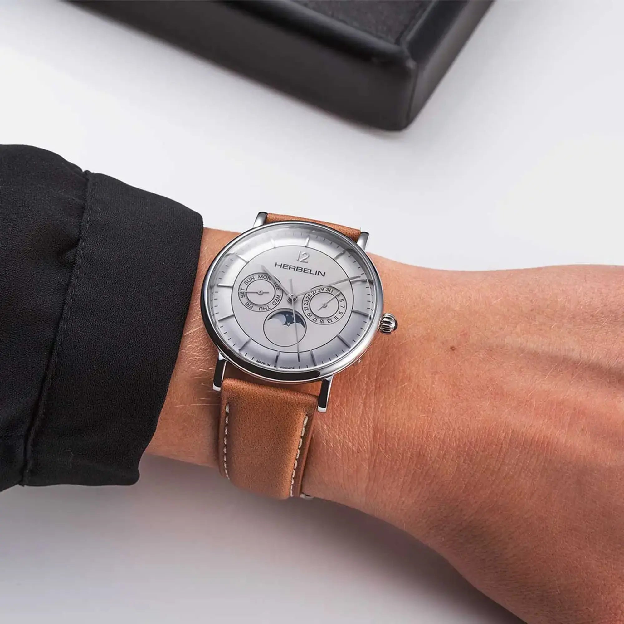 Au poignet masculin, cadran argent blanc brossé et bracelet cuir visibles