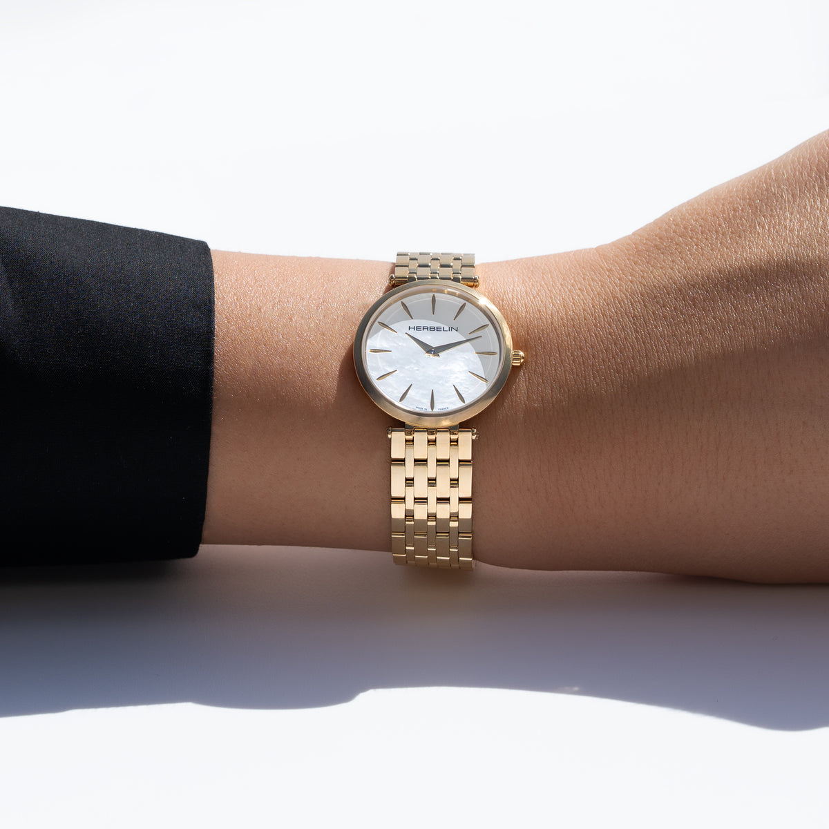Al polso femminile, quadrante in madreperla bianca e bracciale in acciaio PVD oro giallo visibili