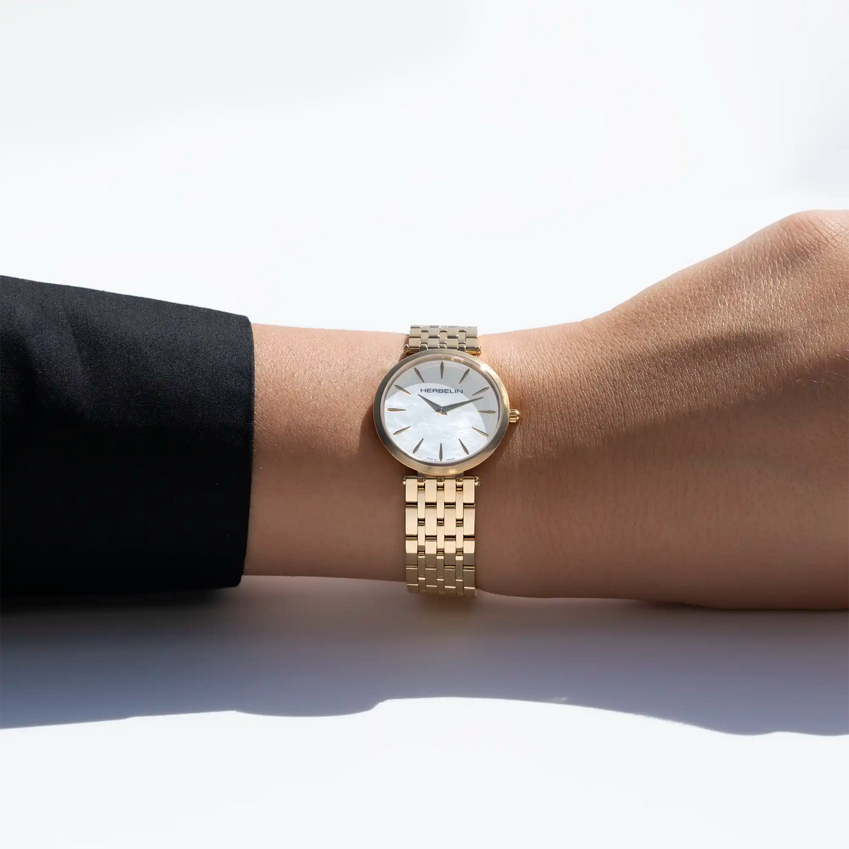 No pulso feminino, visível mostrador em madrepérola branca e bracelete em aço PVD ouro amarelo