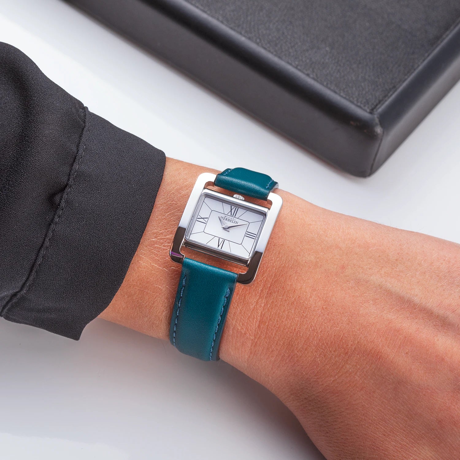 Au poignet féminin, cadran nacre blanche et bracelet cuir bleu-vert visibles