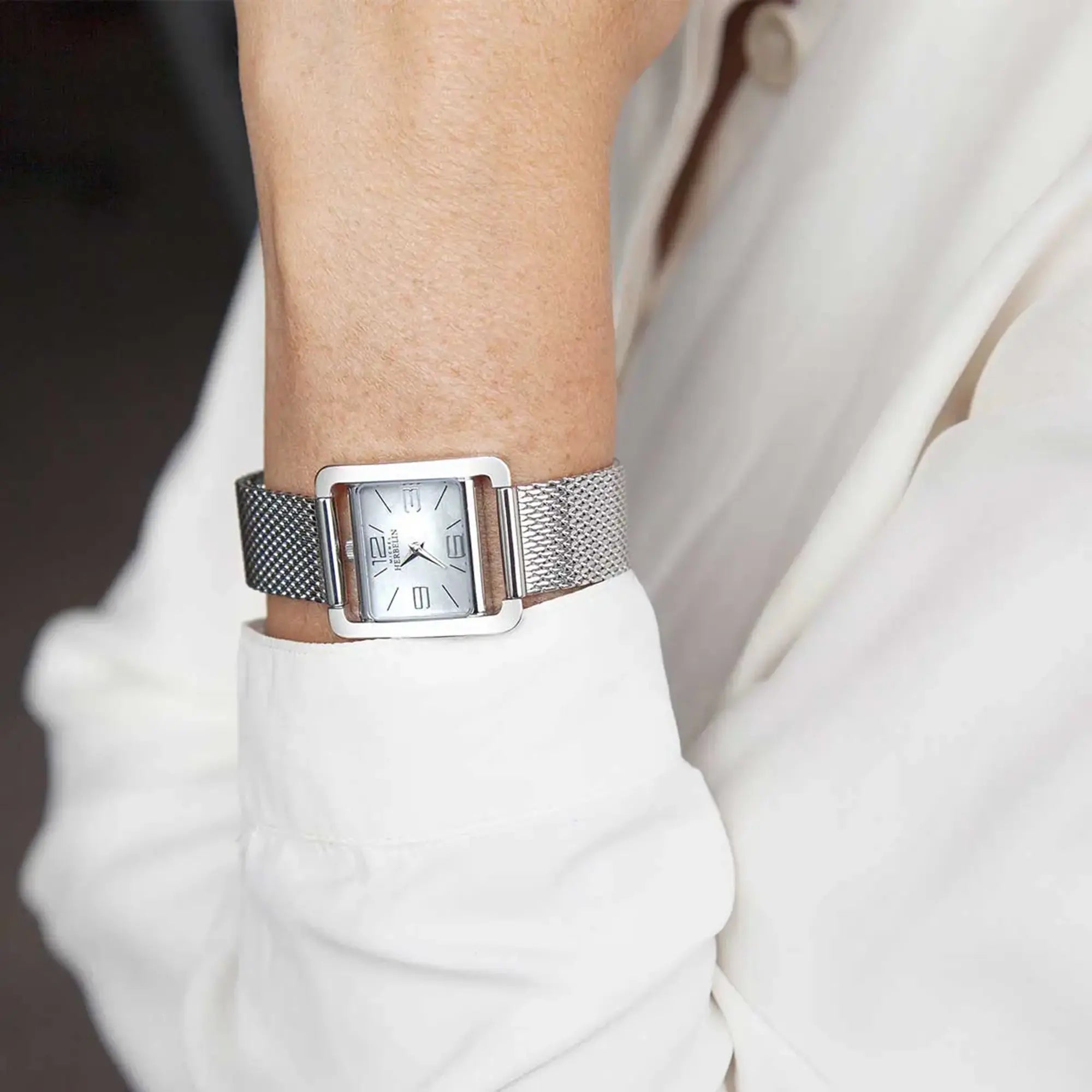 Au poignet féminin, cadran nacre blanche et bracelet acier visibles