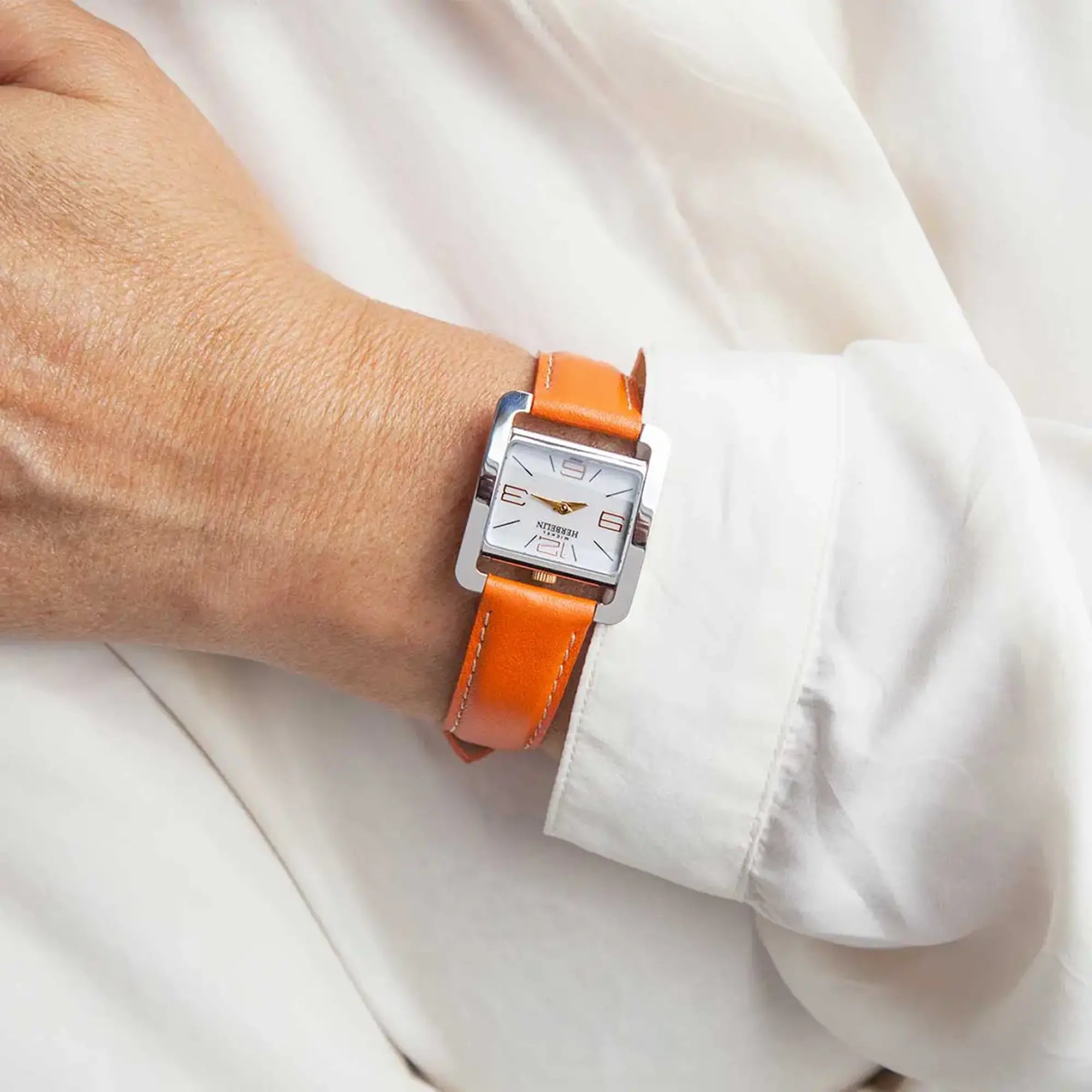 Au poignet féminin, cadran blanc laqué et bracelet cuir visibles