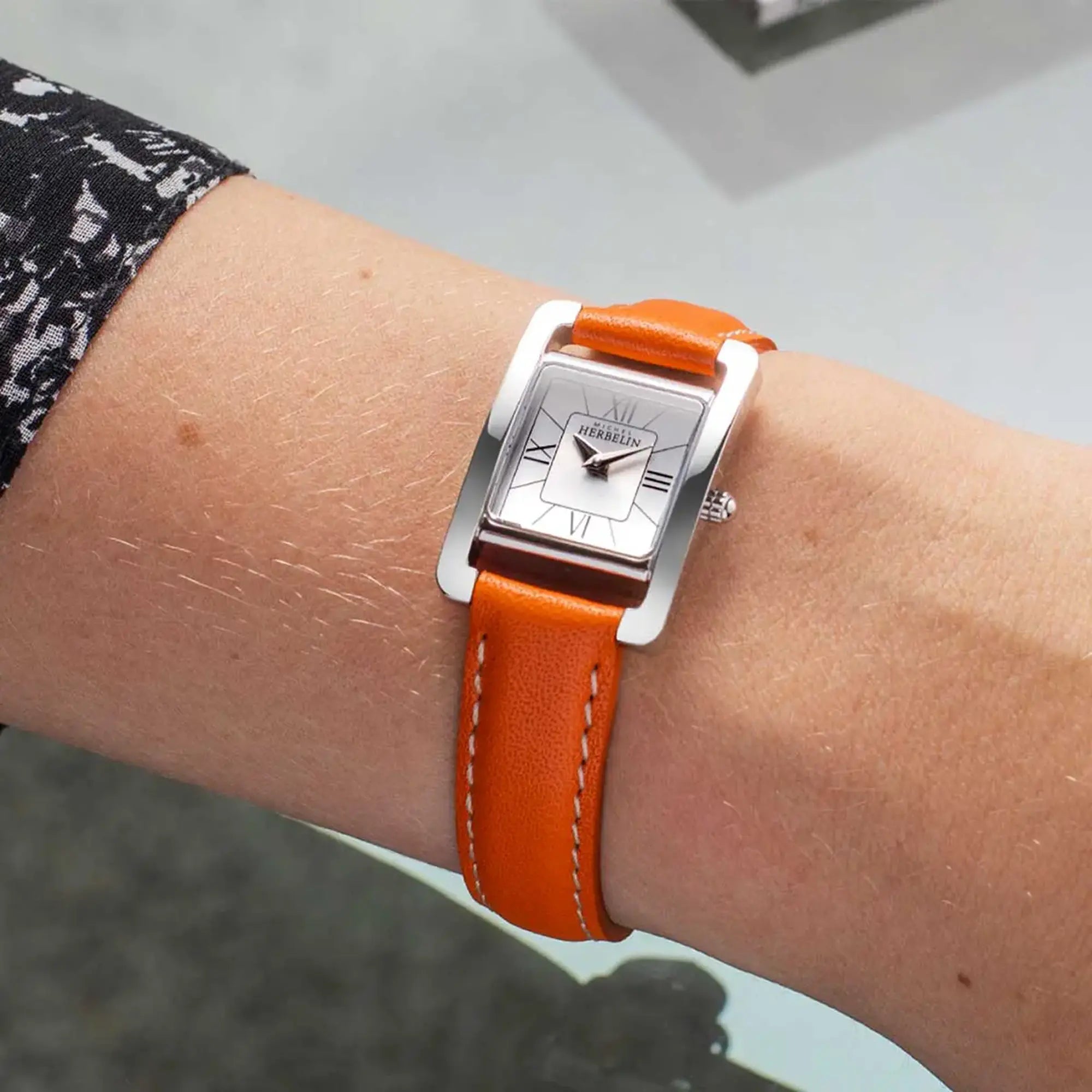 Au poignet féminin, cadran argent et bracelet cuir visibles