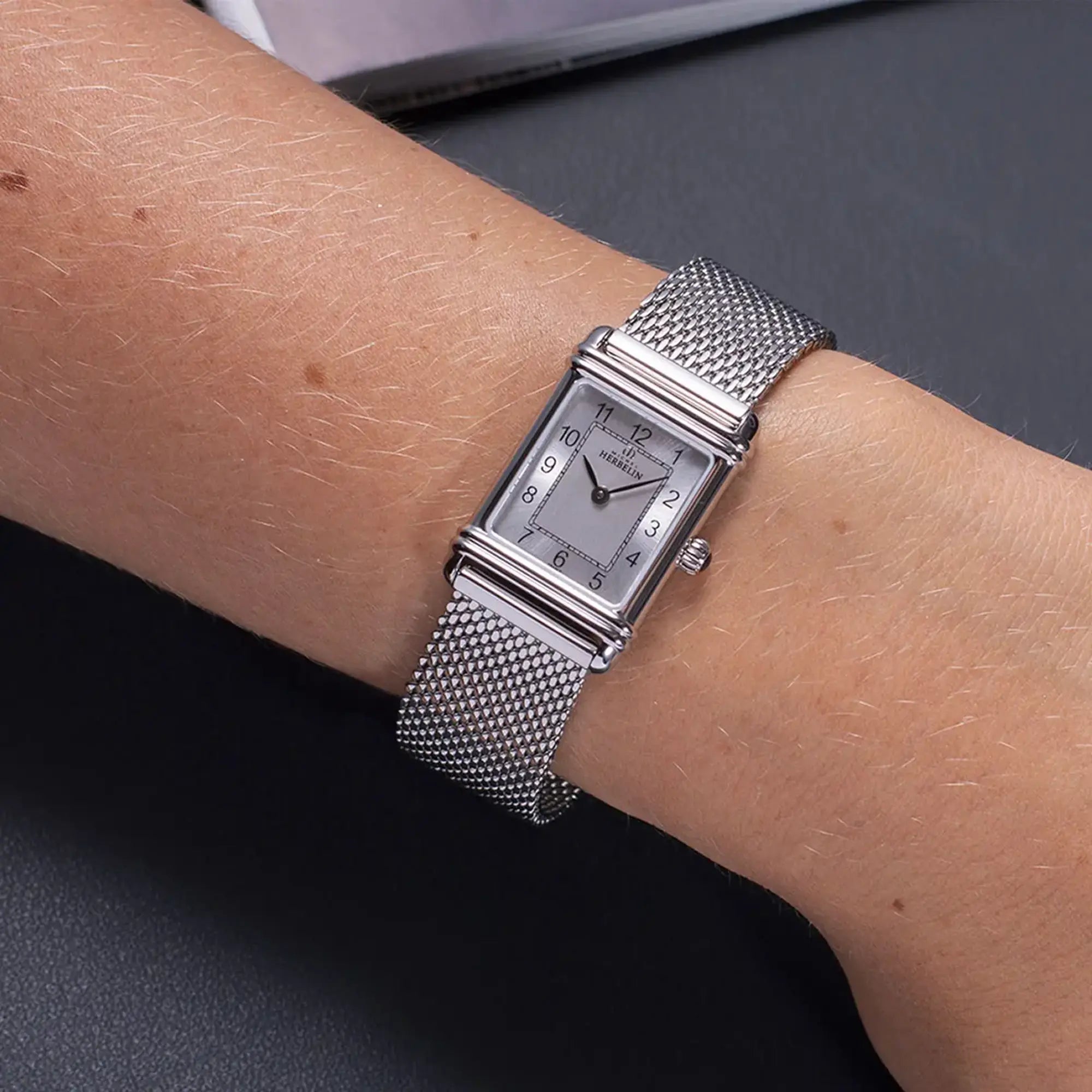 Au poignet féminin, cadran argent brossé vertical et bracelet acier visibles