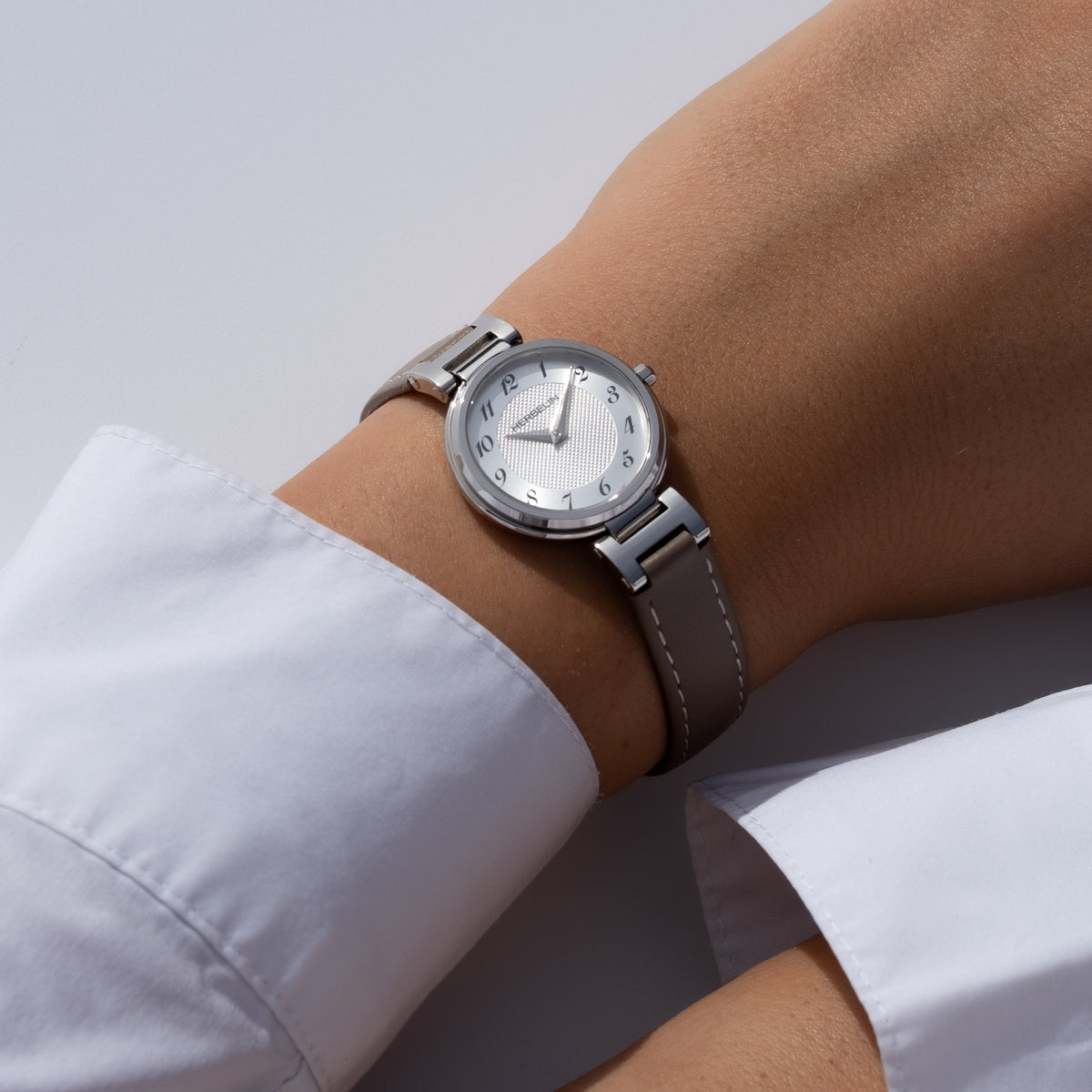 Au poignet féminin, cadran argent blanc guilloché et bracelet cuir visibles