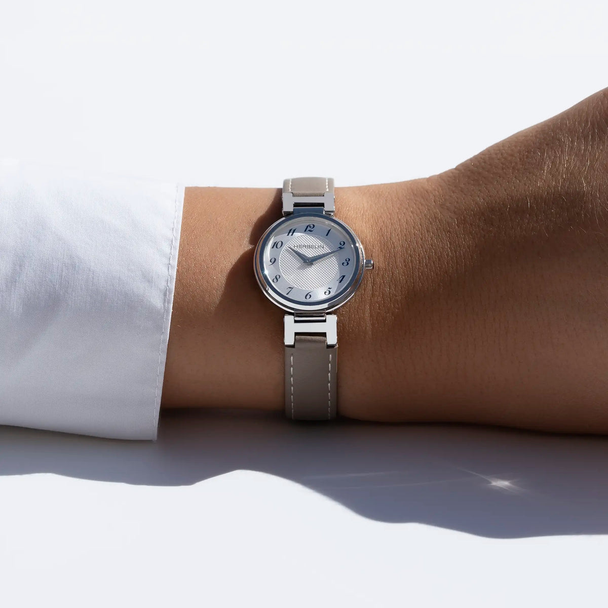 En la muñeca femenina, esfera plateada blanca guilloché y brazalete de piel visibles