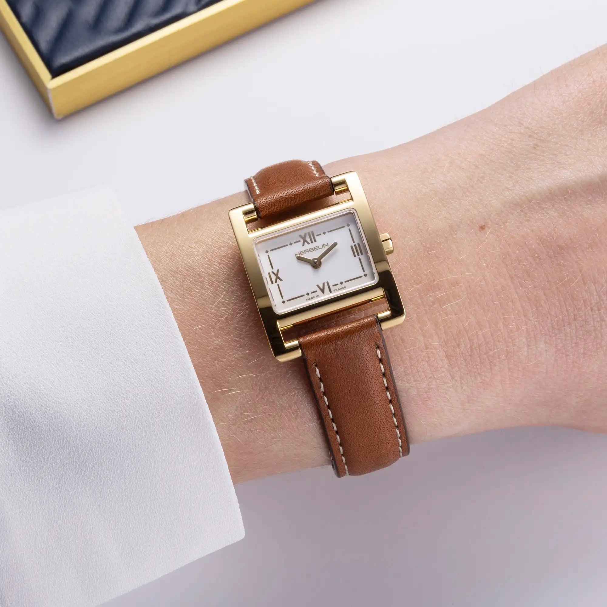 Au poignet féminin, cadran blanc laqué et bracelet cuir visibles