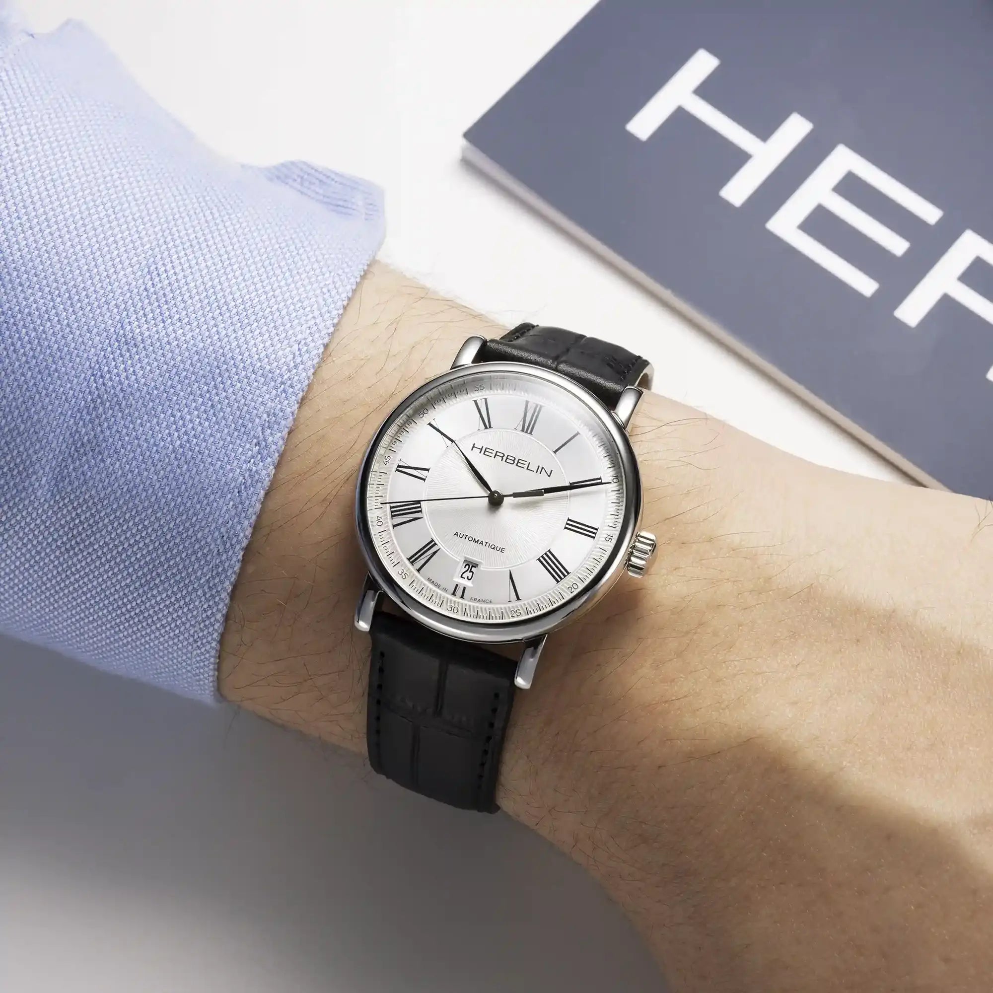 Au poignet masculin, cadran argent guilloché et bracelet cuir visibles