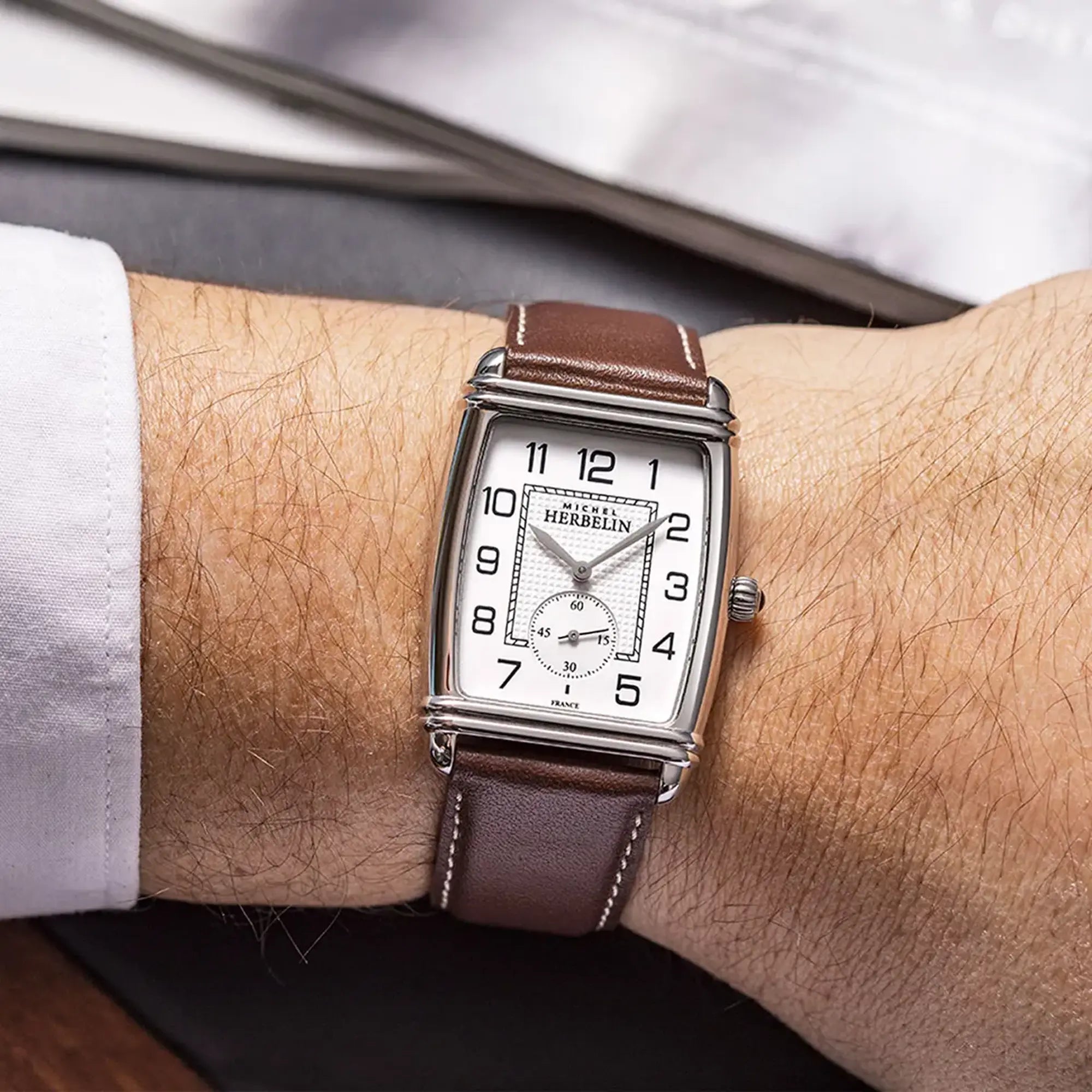 Au poignet masculin, cadran argent guilloché et bracelet cuir visibles