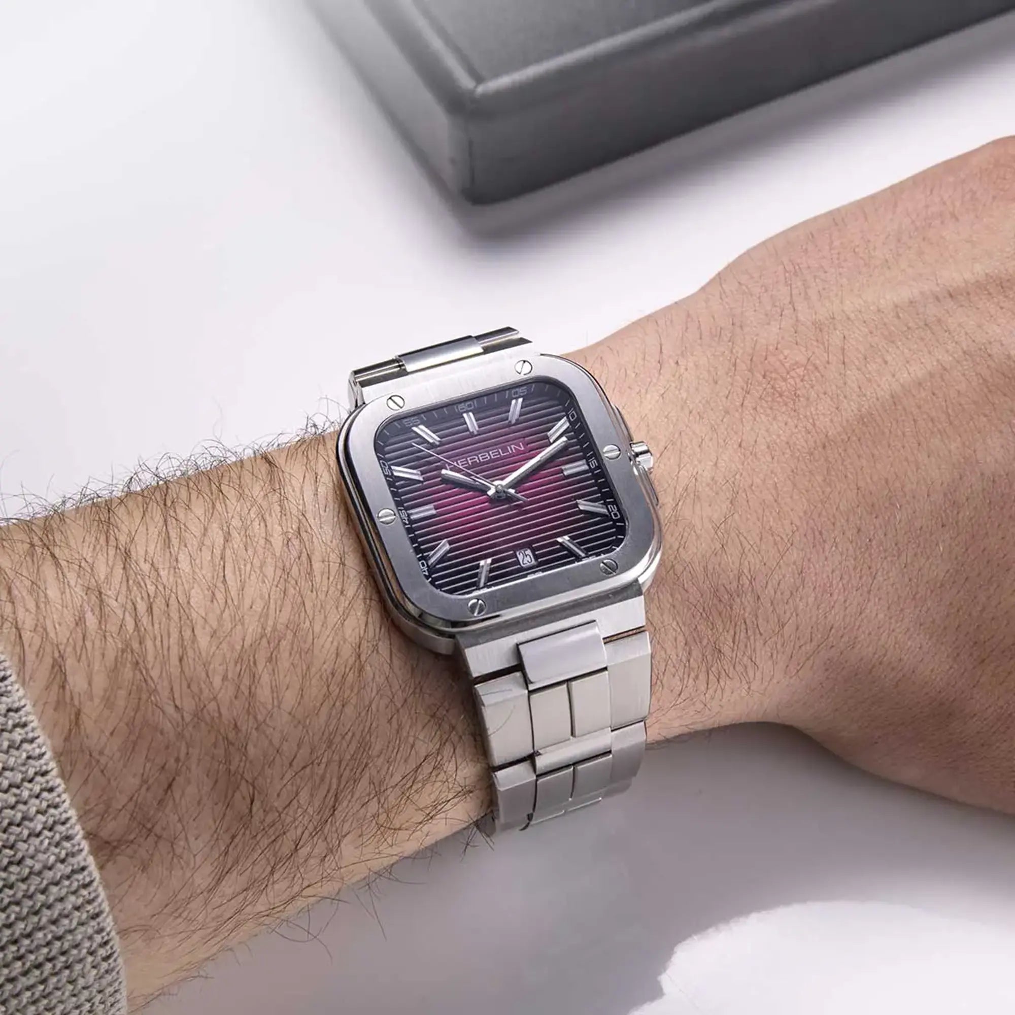 Au poignet masculin, cadran bordeaux dégradé et bracelet acier visibles