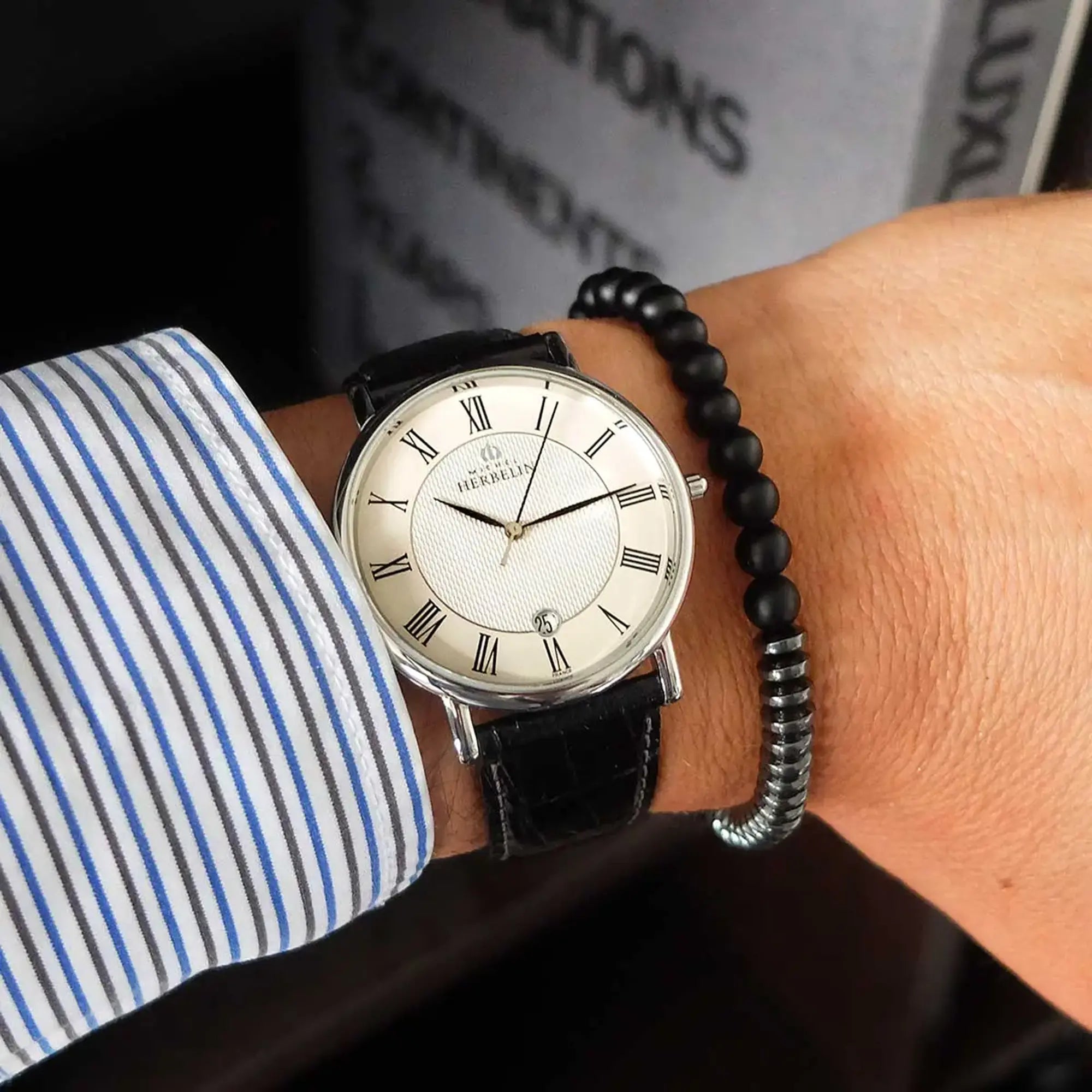 Au poignet masculin, cadran argent guilloché et bracelet cuir visibles