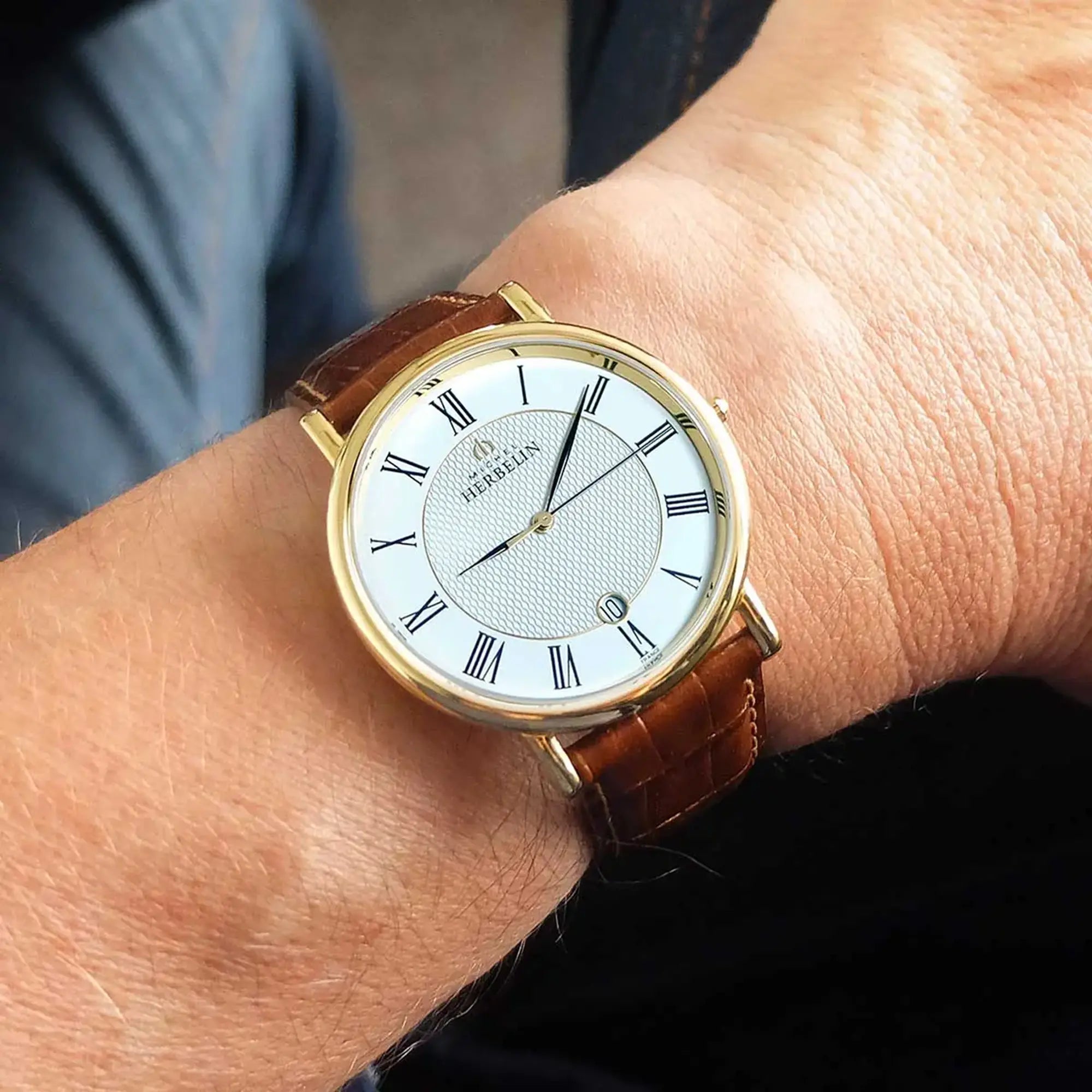 Au poignet masculin, cadran argent guilloché et bracelet cuir visibles