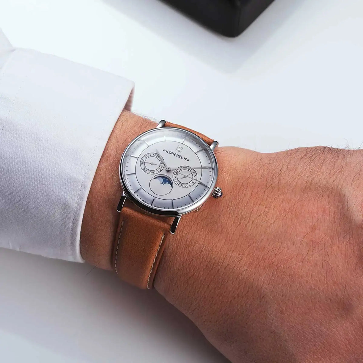 ⁣⁢On a masculine wrist, a brushed white silver dial and leather strap are visible⁤⁣