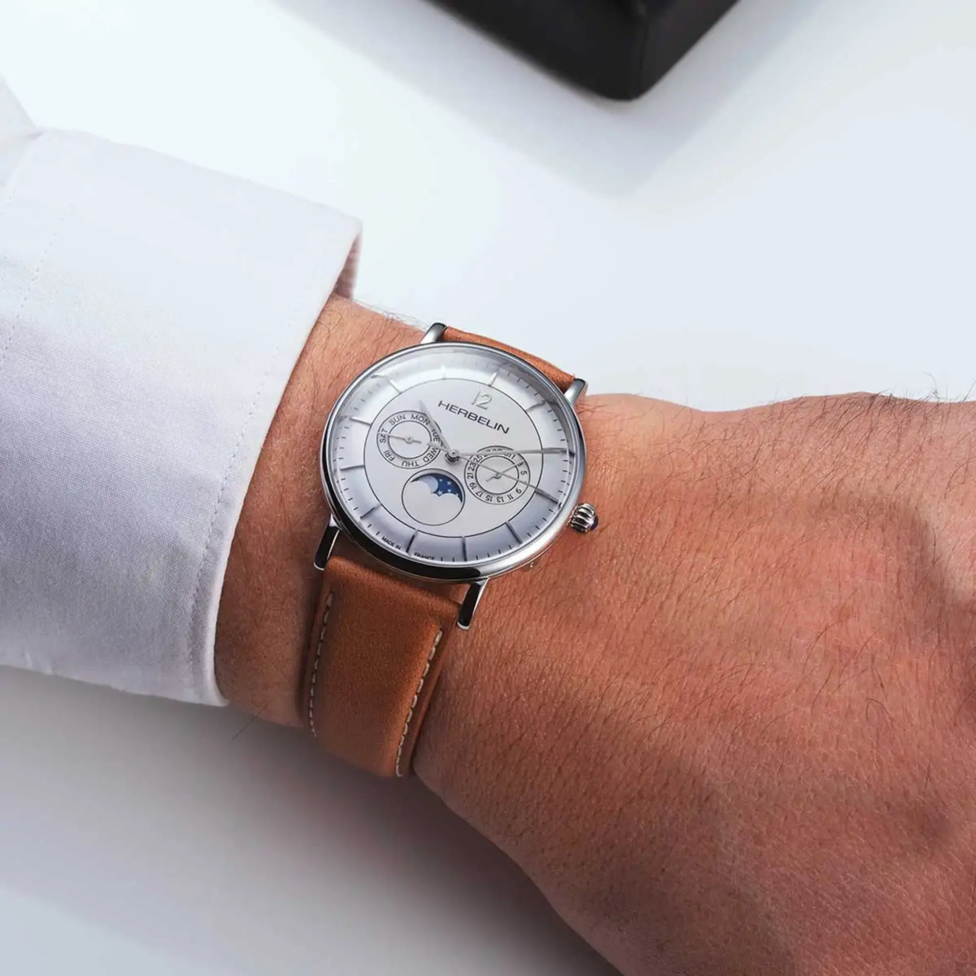 Au poignet masculin, cadran argent blanc brossé et bracelet cuir visibles