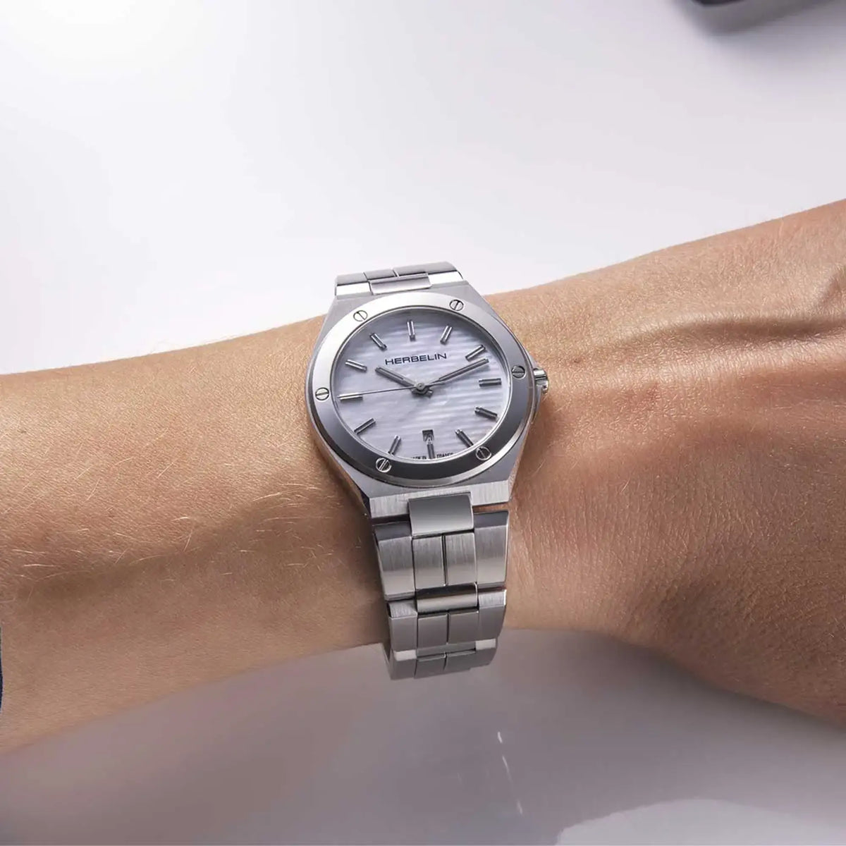 ⁣⁢On a feminine wrist, the white mother-of-pearl dial and steel bracelet are visible⁤⁣