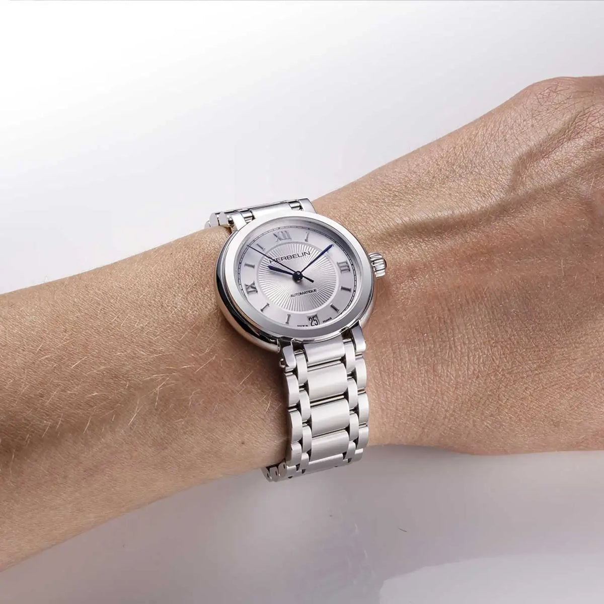 ⁣⁢En muñeca femenina, esfera plateada guilloché y brazalete de acero visibles⁤⁣