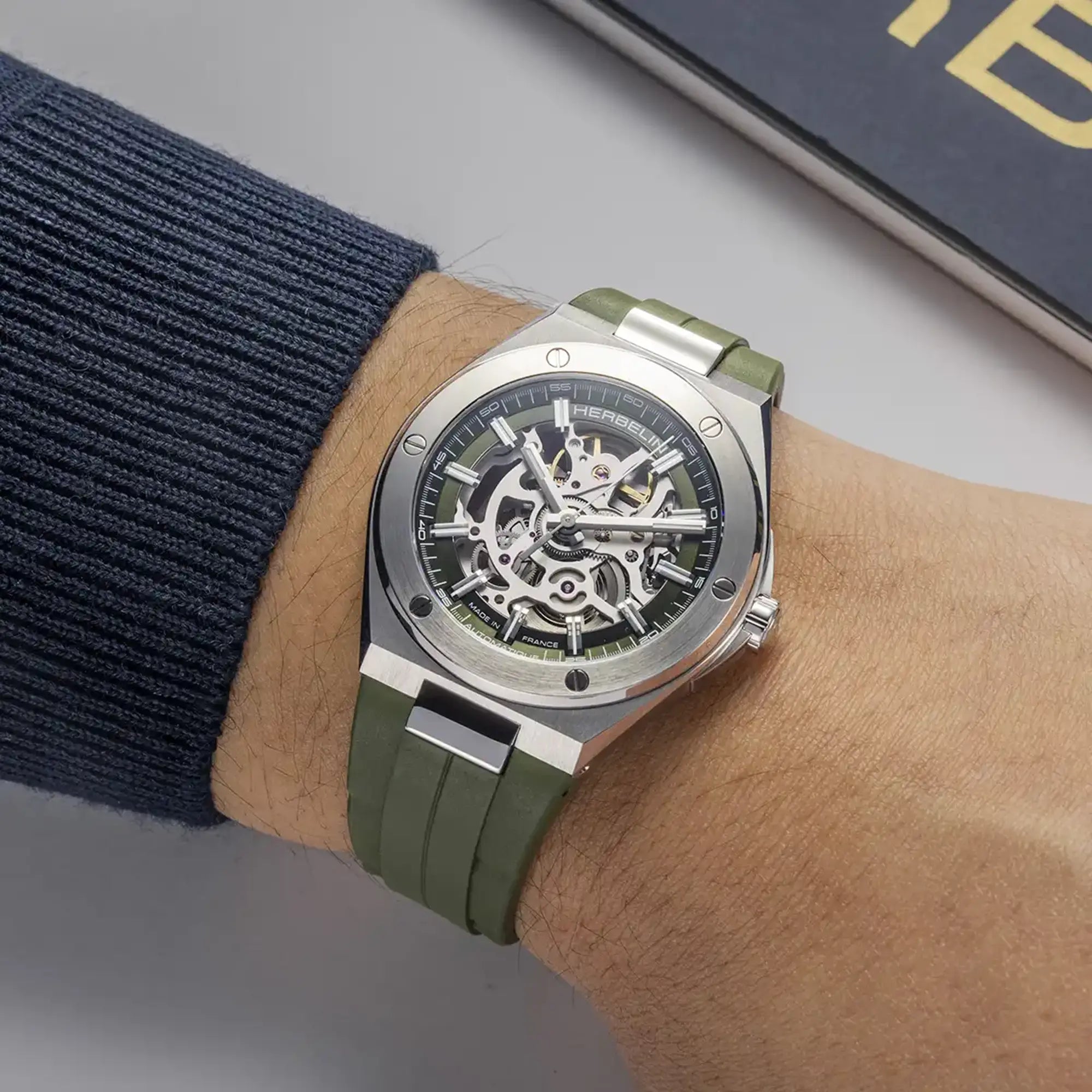 Au poignet masculin, cadran vert kaki et bracelet caoutchouc visibles