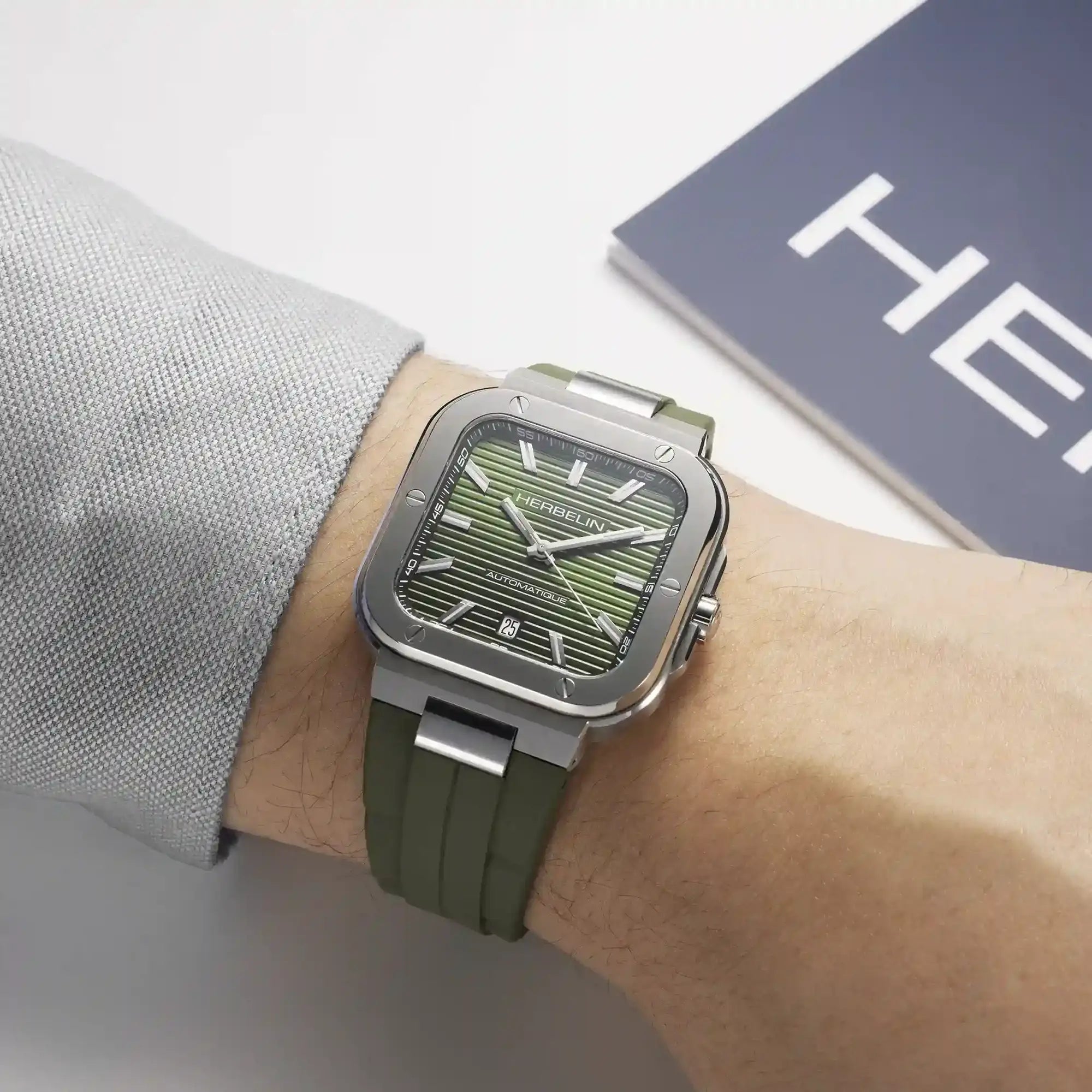 Au poignet masculin, cadran vert kaki et bracelet caoutchouc visibles