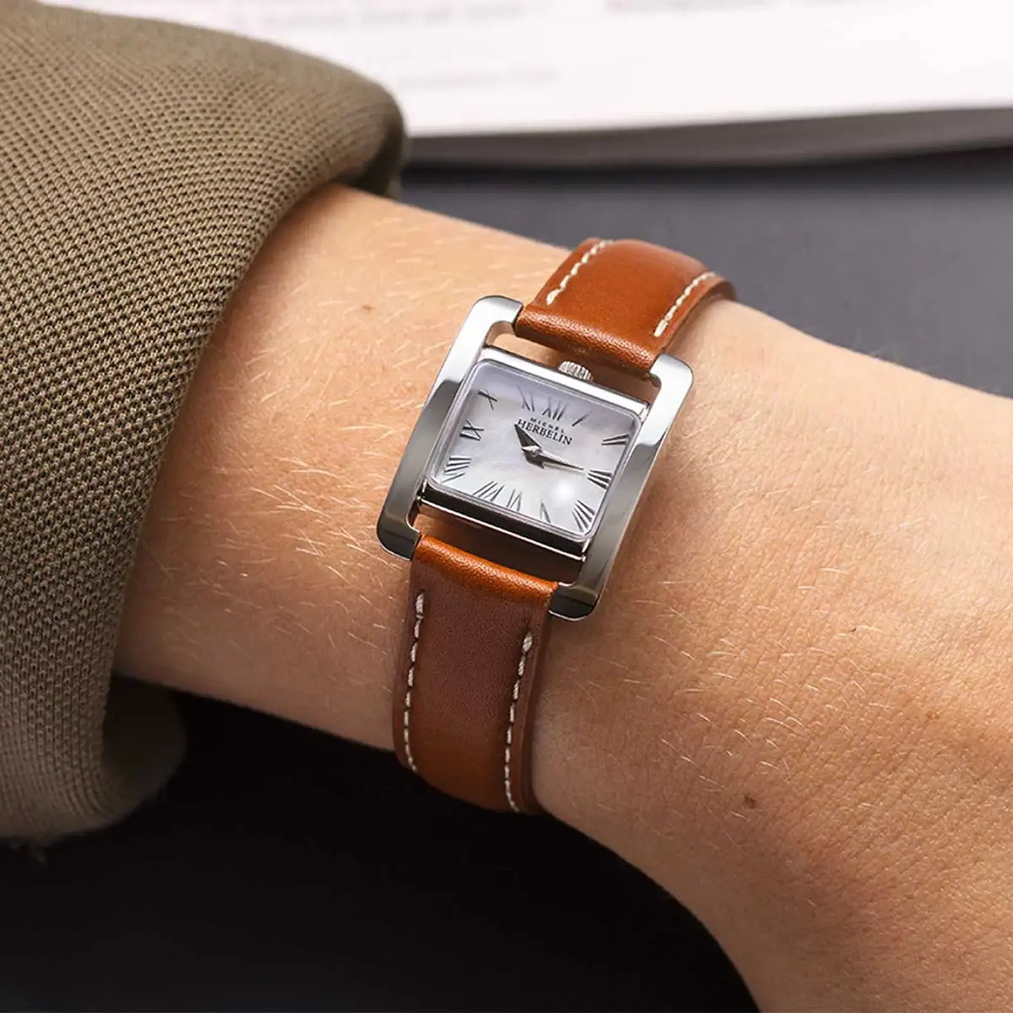 Au poignet féminin, cadran nacre blanche et bracelet cuir visibles