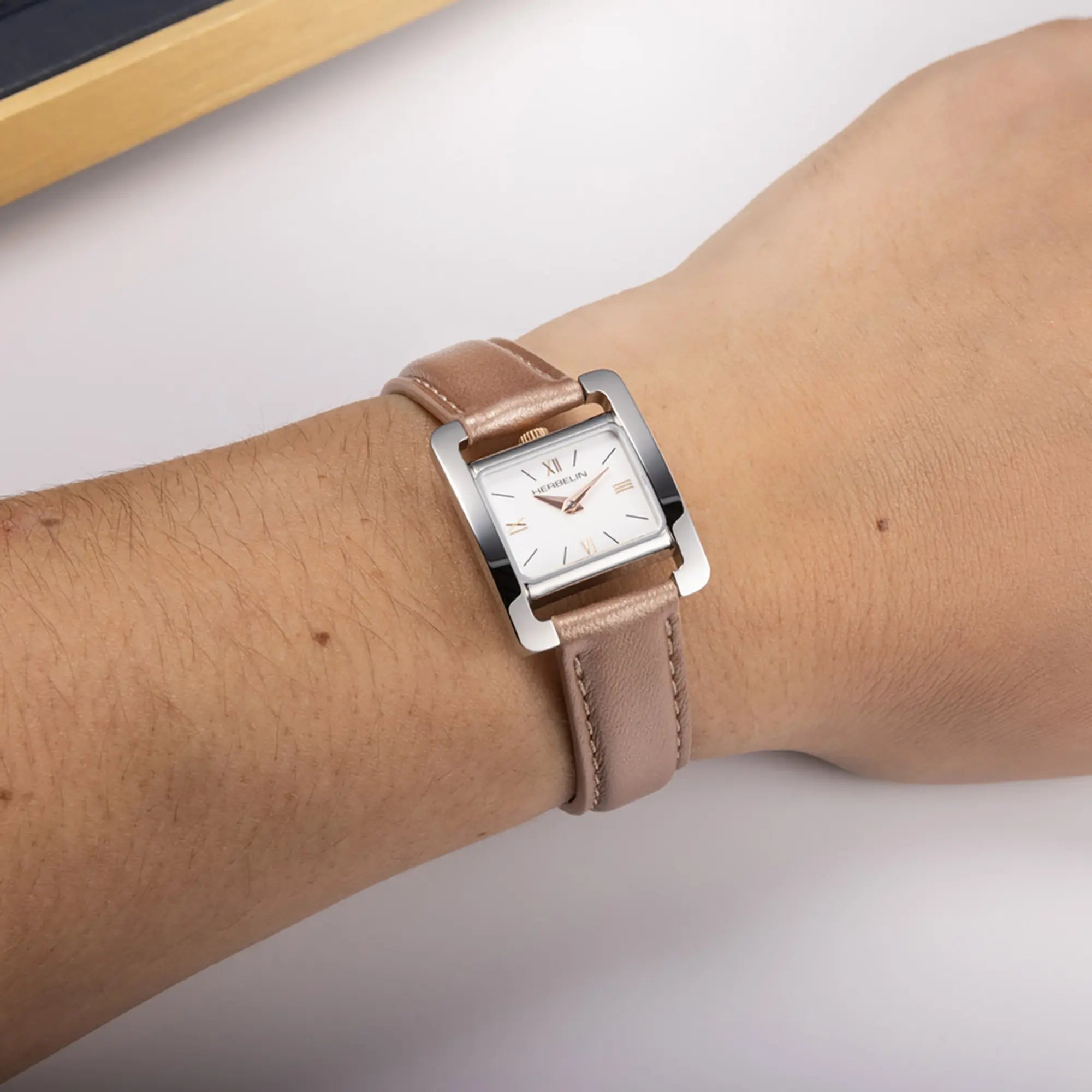 Au poignet féminin, cadran blanc laqué et bracelet cuir visibles