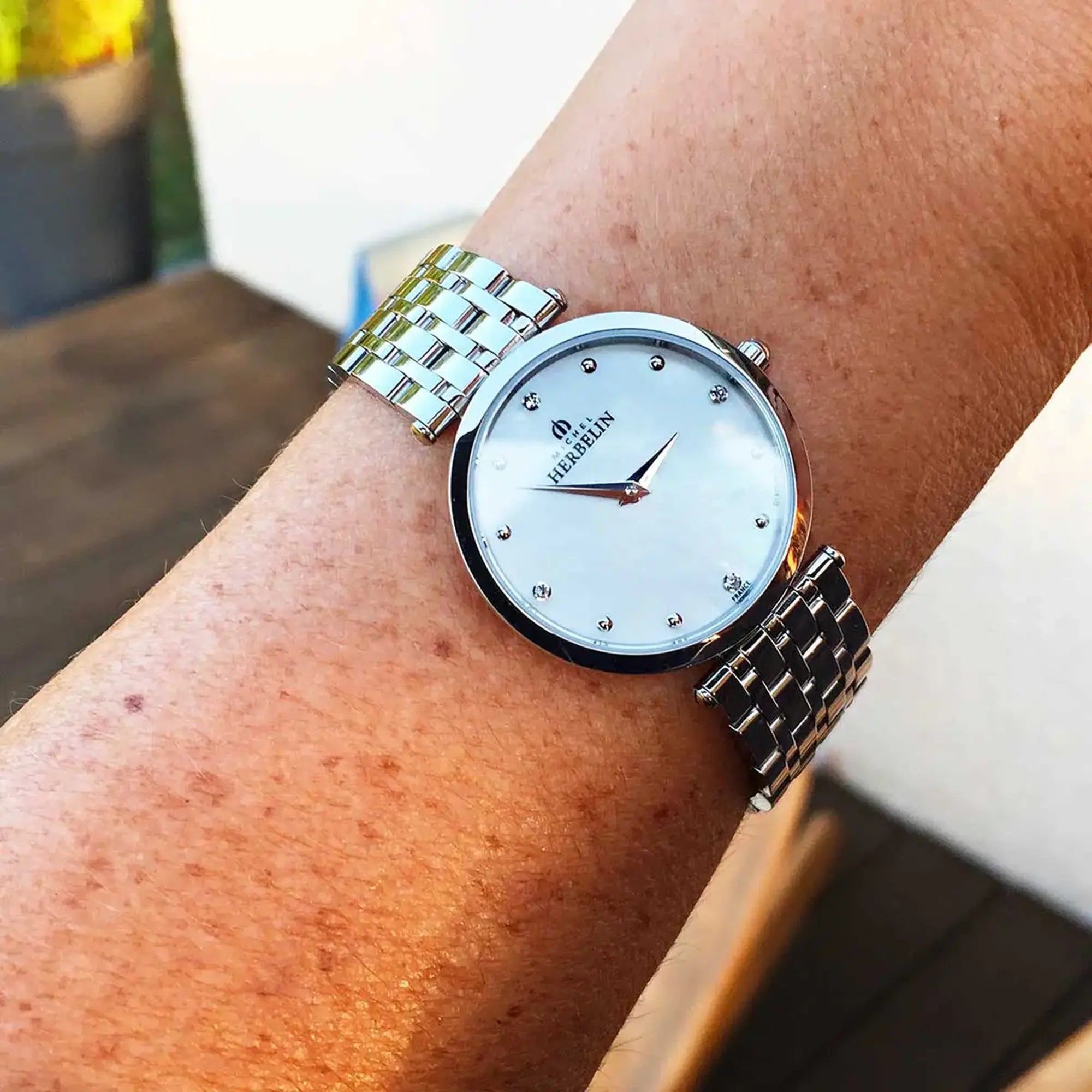 Au poignet féminin, cadran nacre blanche et bracelet acier visibles