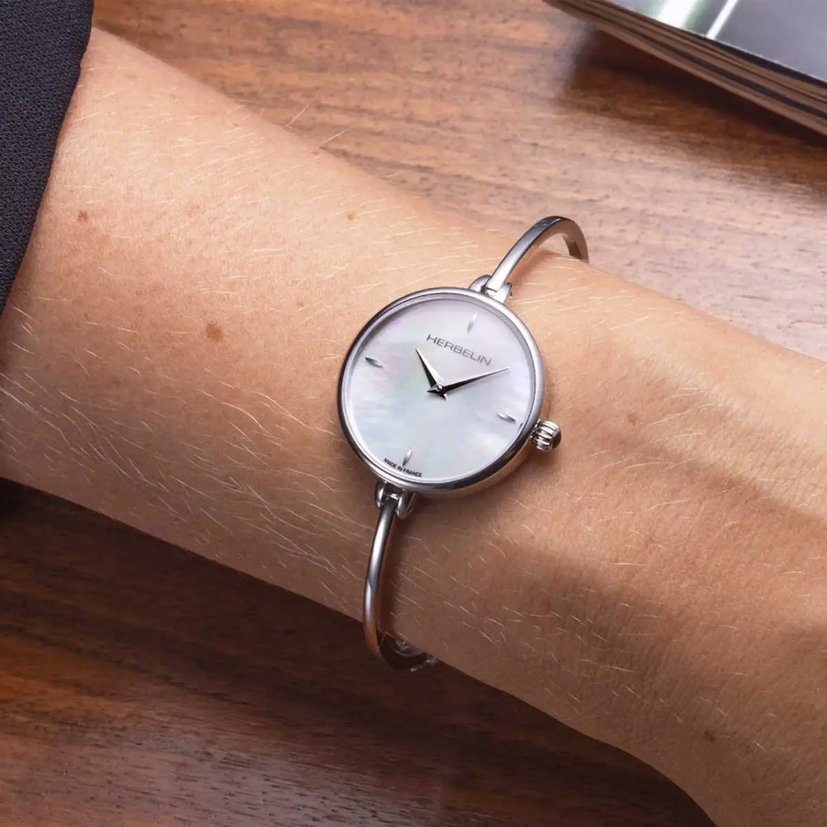 ⁣⁢On a feminine wrist, the white mother-of-pearl dial and steel bracelet are visible⁤⁣