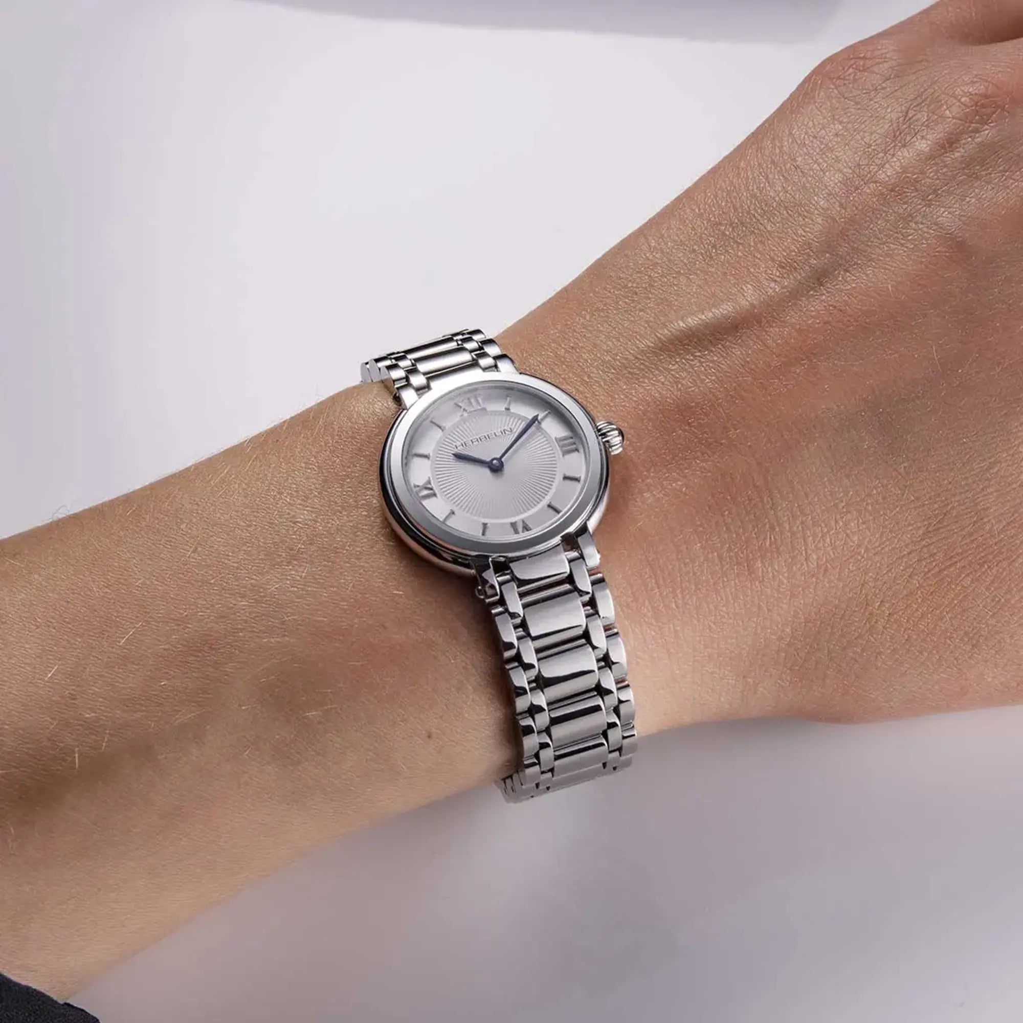 Au poignet féminin, cadran argent guilloché et bracelet acier visibles