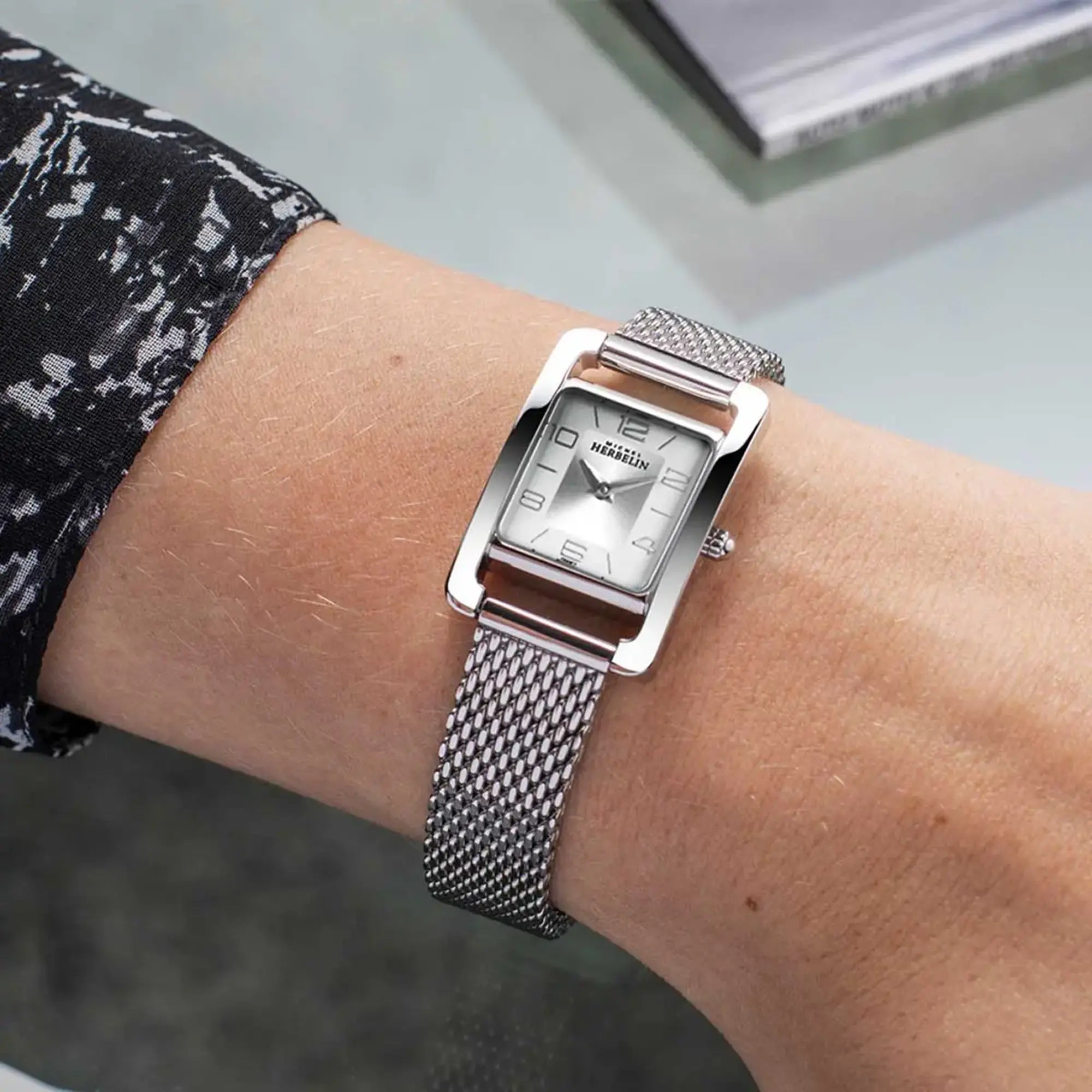 Au poignet féminin, cadran argent brossé vertical et bracelet acier visibles