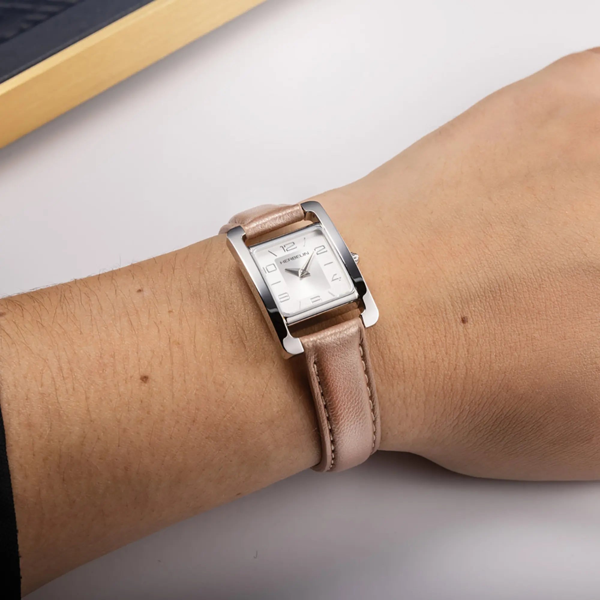 Au poignet féminin, cadran argent et bracelet cuir visibles