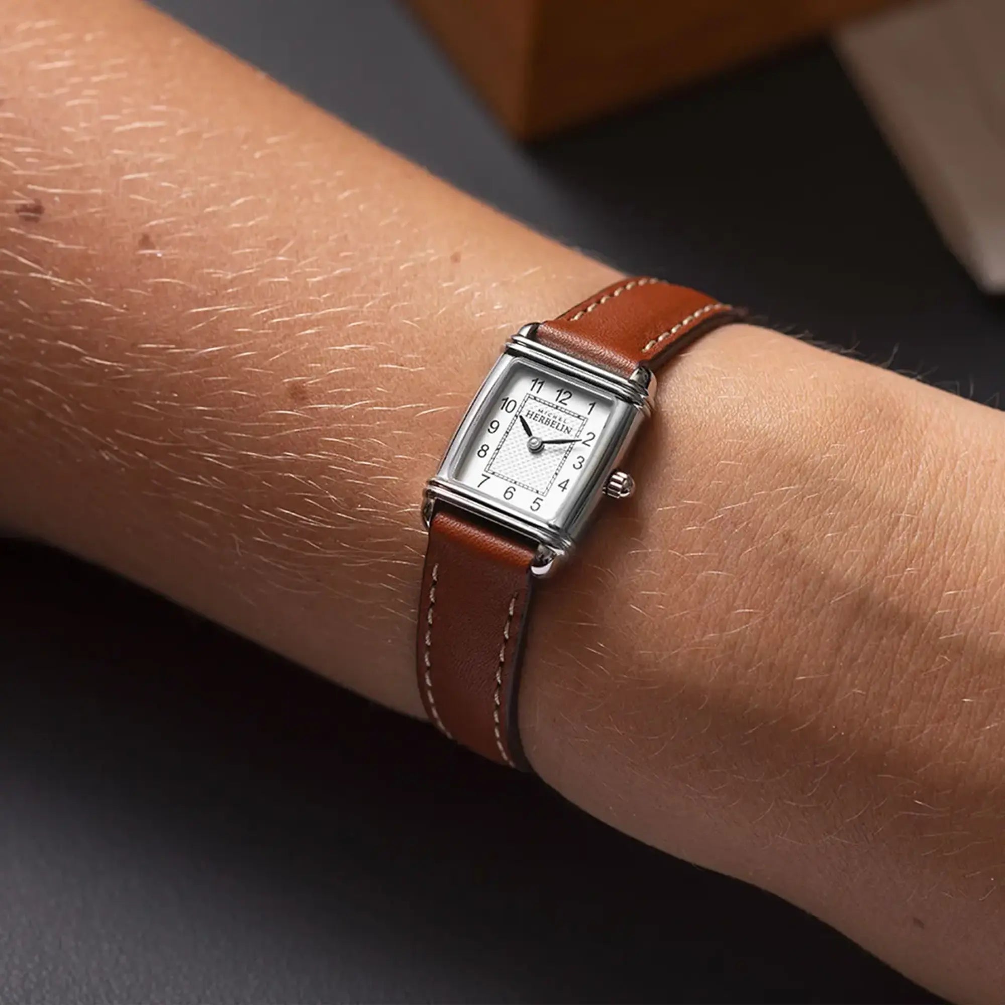 Au poignet féminin, cadran argent guilloché et bracelet cuir visibles