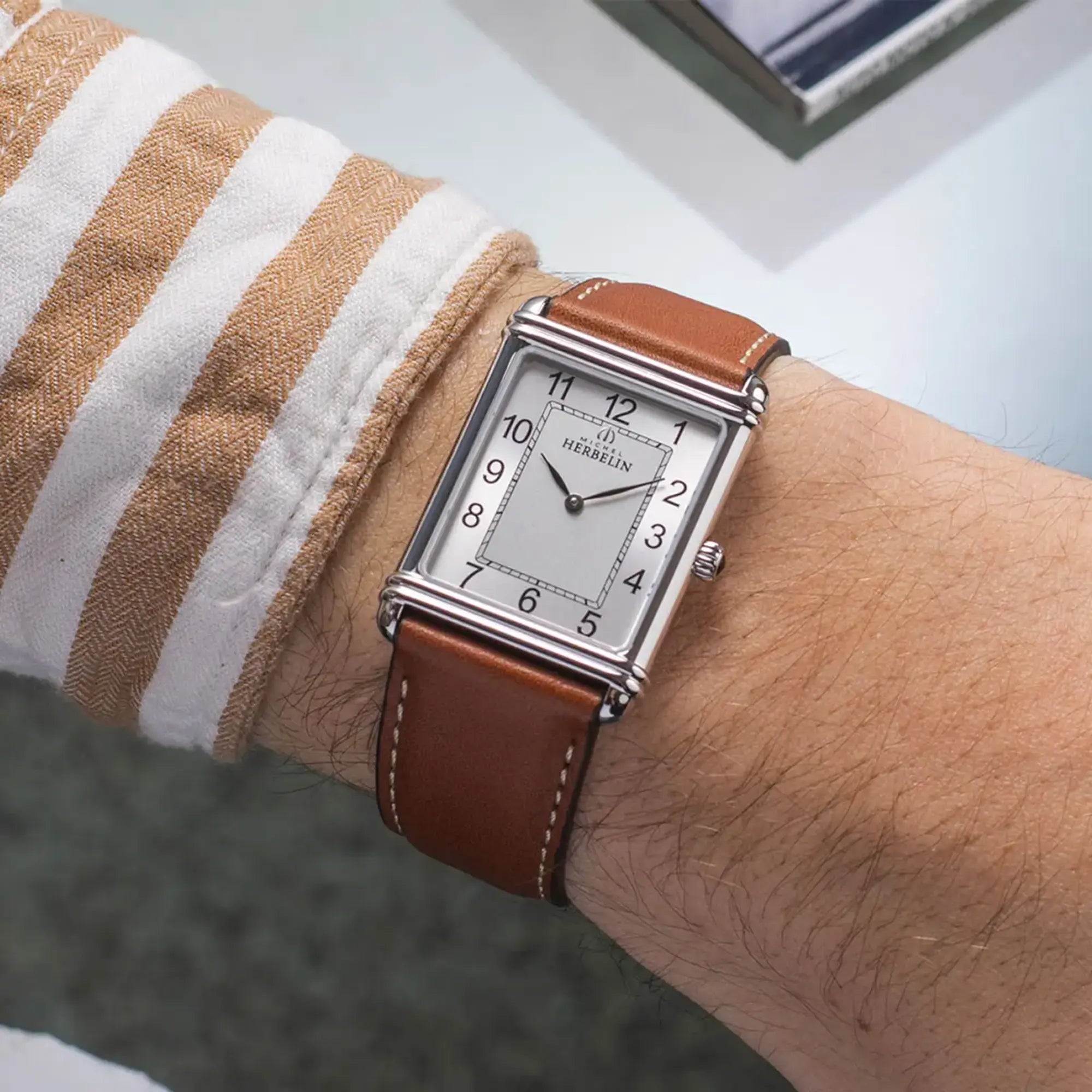 Au poignet masculin, cadran argent brossé vertical et bracelet cuir visibles