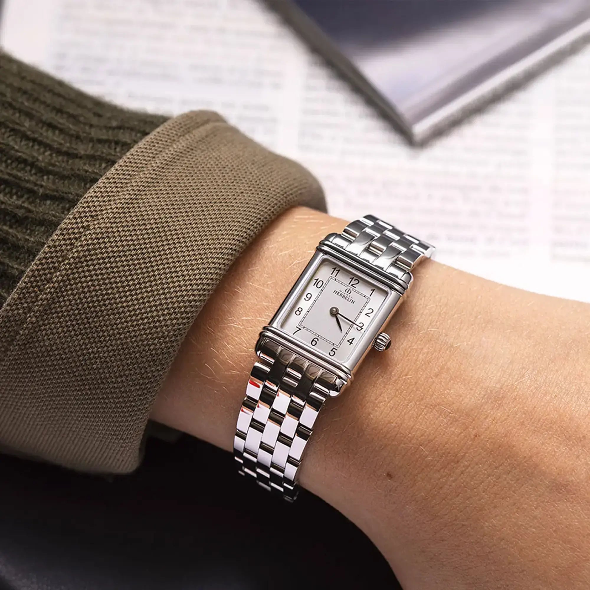 Au poignet féminin, cadran argent brossé vertical et bracelet acier visibles