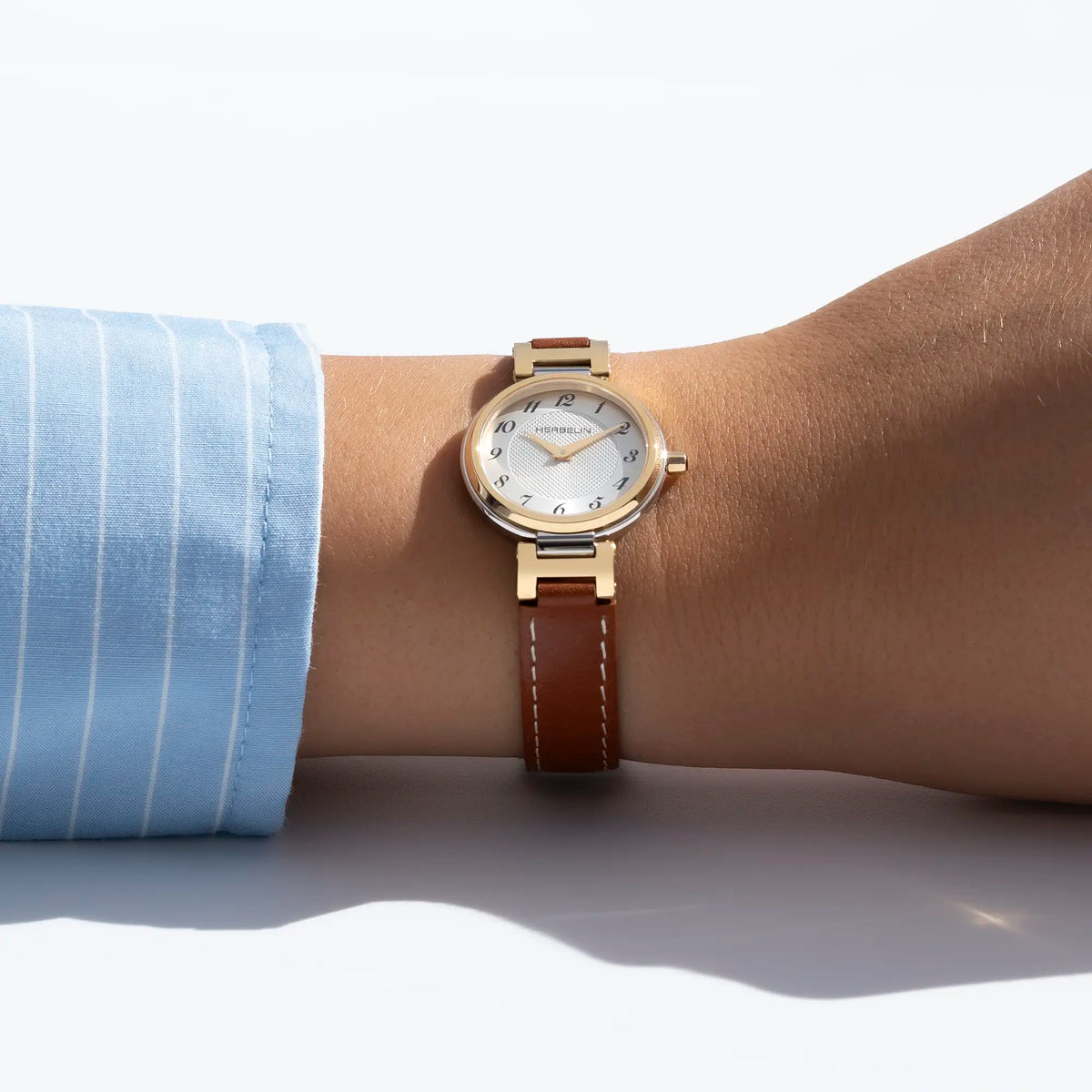 Au poignet féminin, cadran argent blanc guilloché et bracelet cuir visibles
