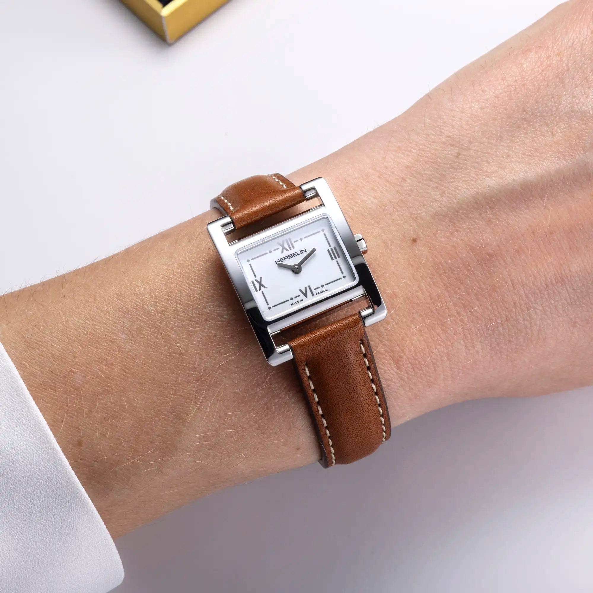 Au poignet féminin, cadran blanc laqué et bracelet cuir visibles