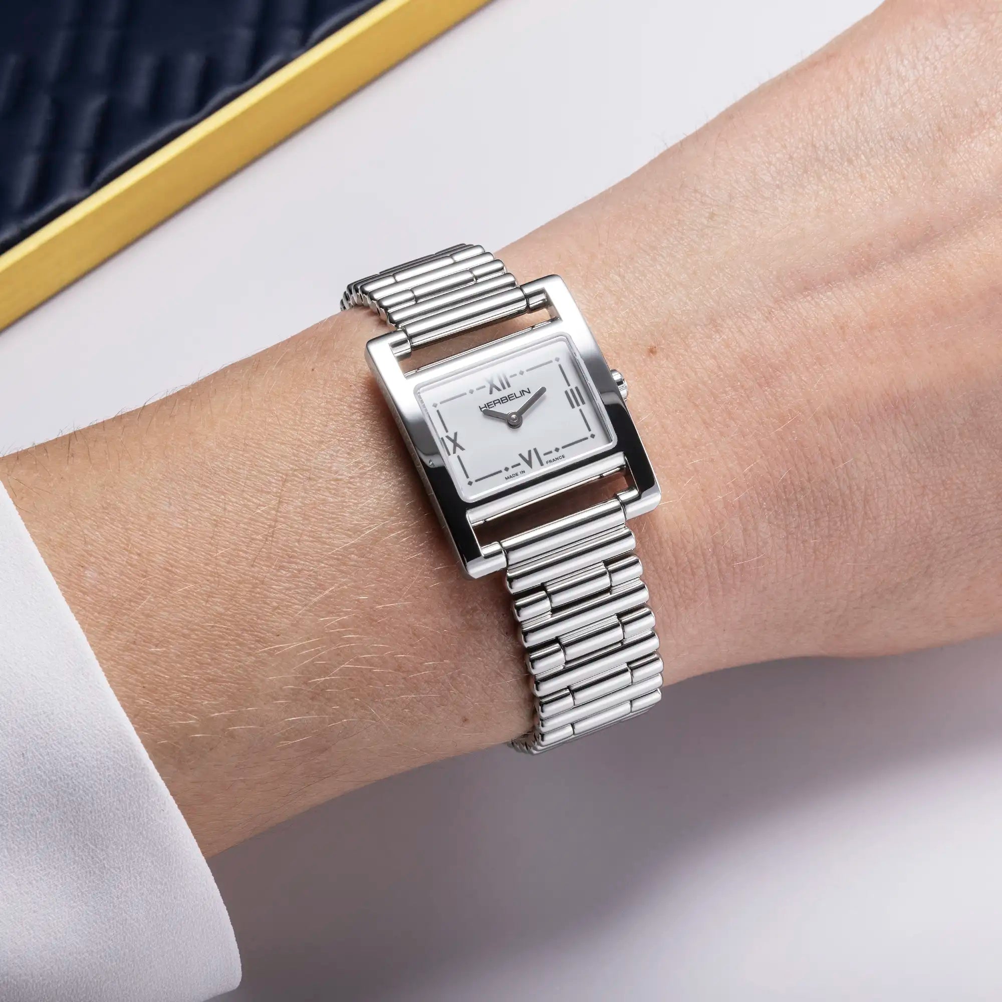 Au poignet féminin, cadran blanc laqué et bracelet acier visibles