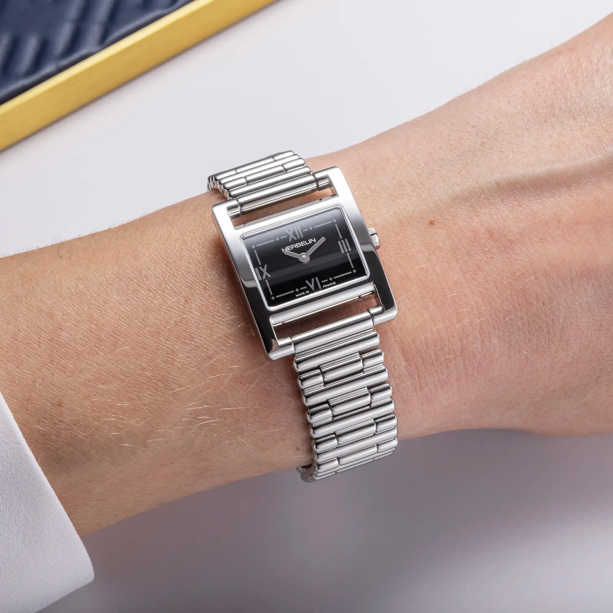 Au poignet féminin, cadran laqué noir et bracelet acier visibles