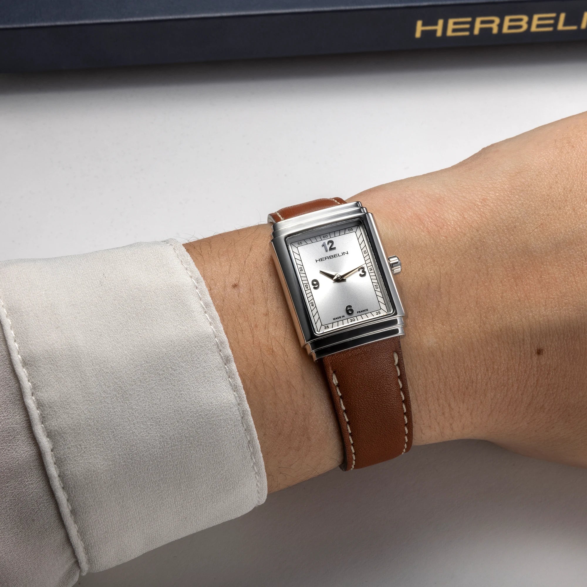 Au poignet féminin, cadran argenté et bracelet cuir camel visibles