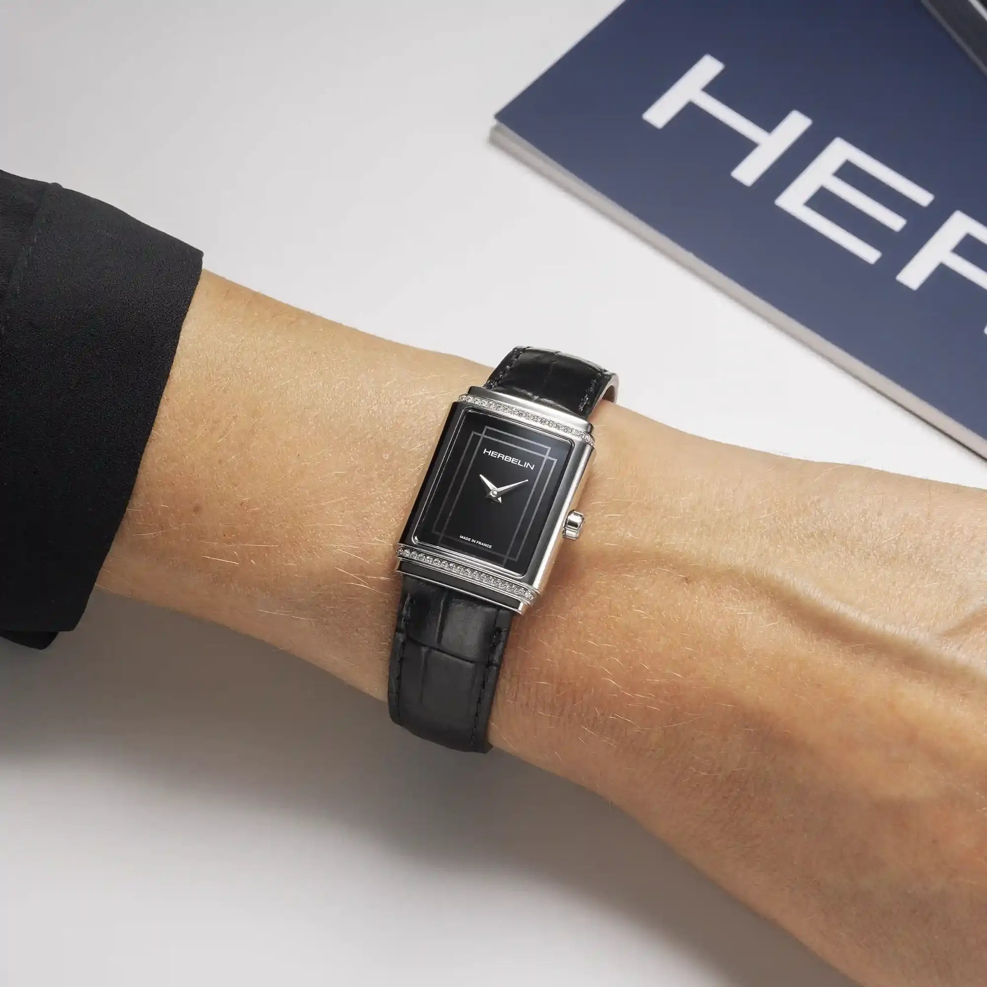 Au poignet féminin, cadran laqué noir et bracelet cuir visibles