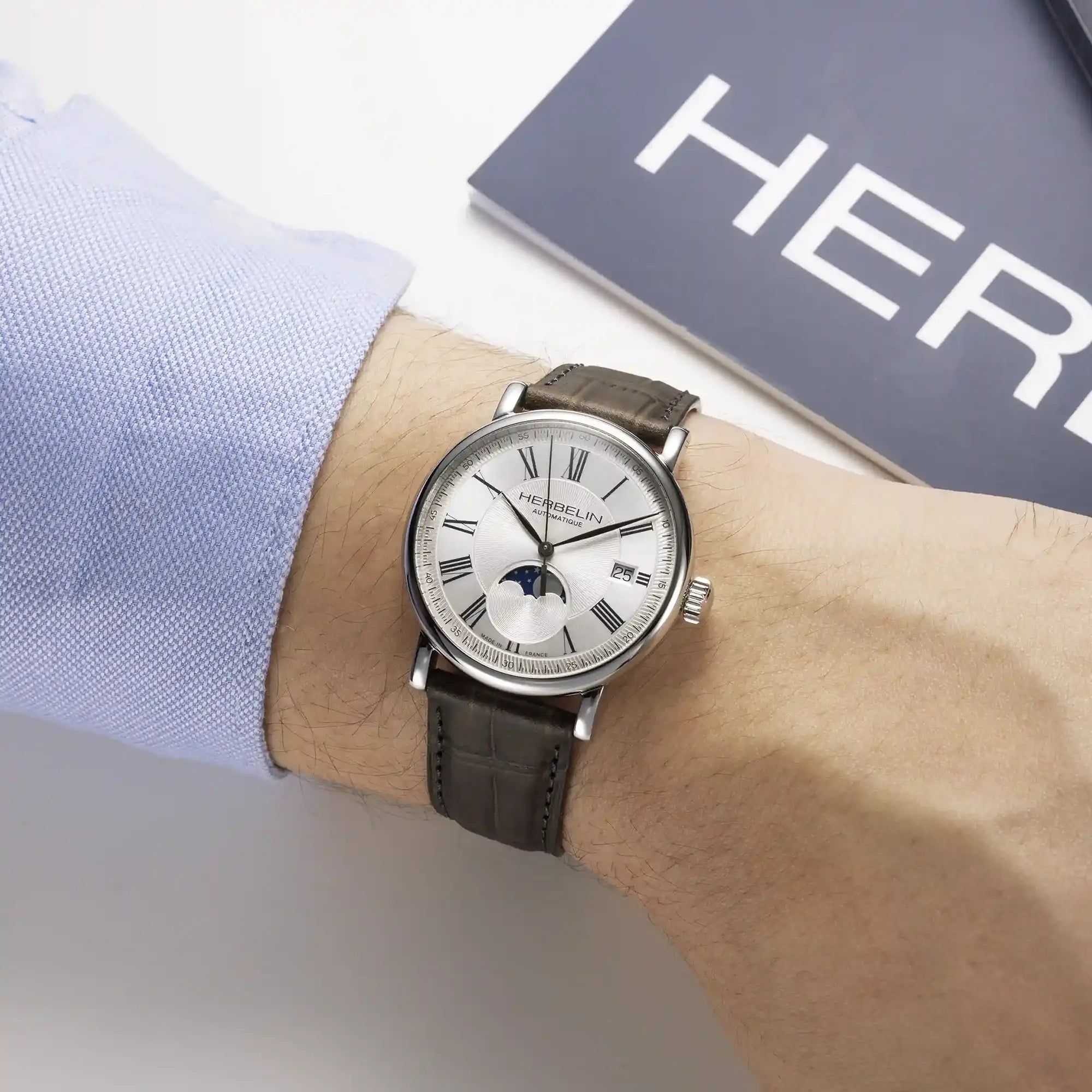 Au poignet masculin, cadran argent guilloché et bracelet cuir visibles
