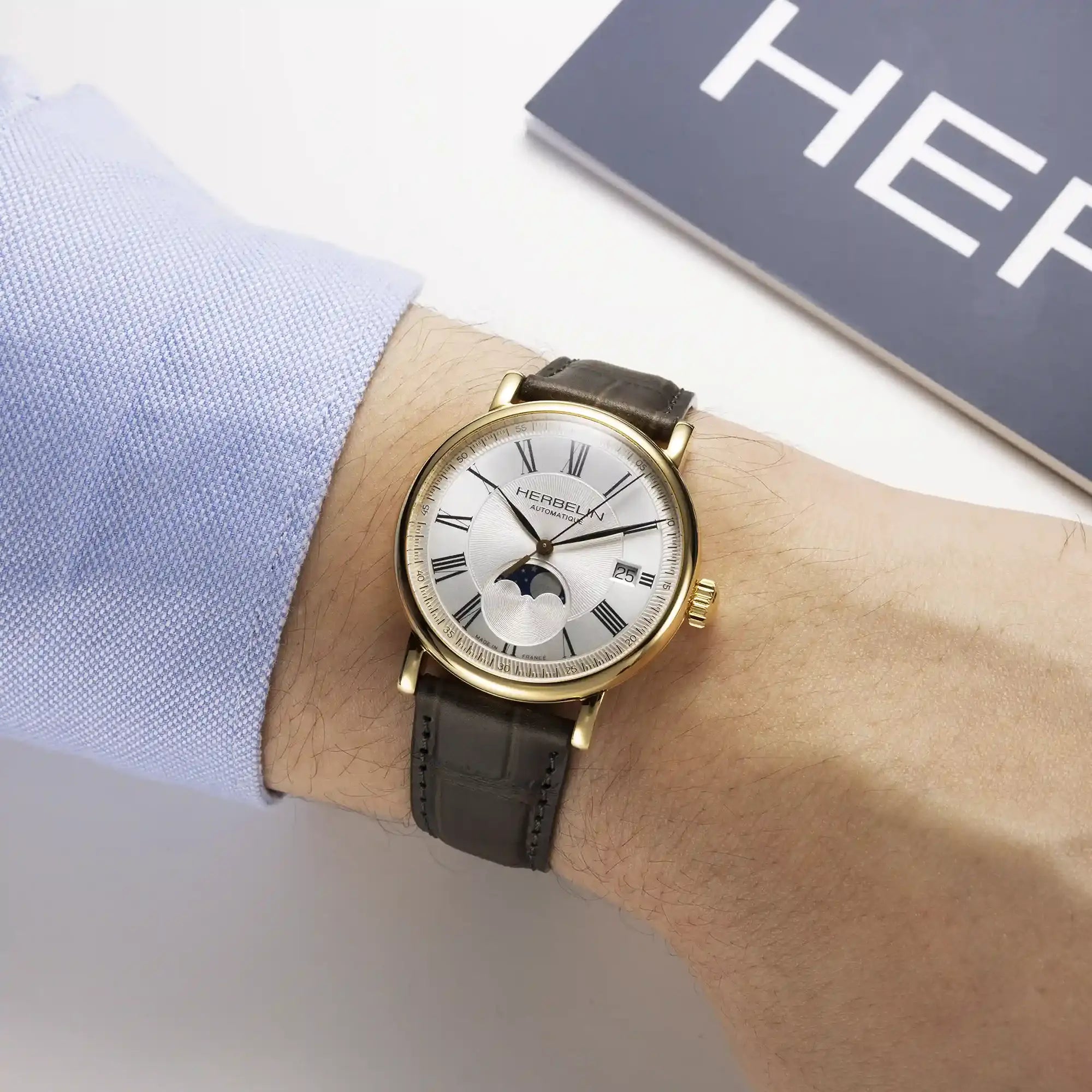 Au poignet masculin, cadran argent guilloché et bracelet cuir visibles