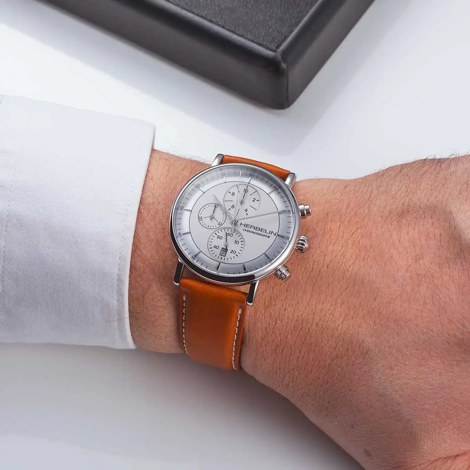Au poignet masculin, cadran argent blanc brossé et bracelet cuir visibles