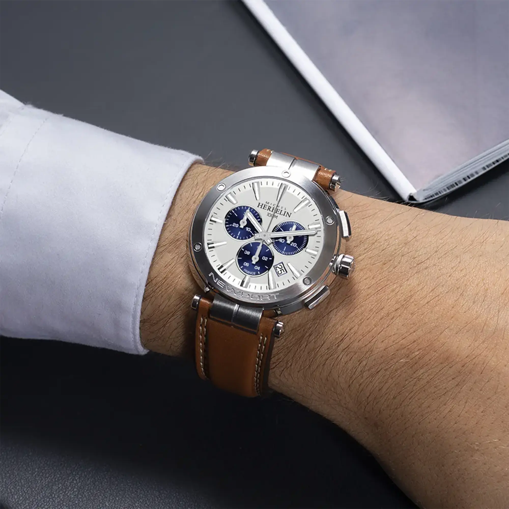 Au poignet masculin, cadran argent blanc brossé et bracelet cuir visibles