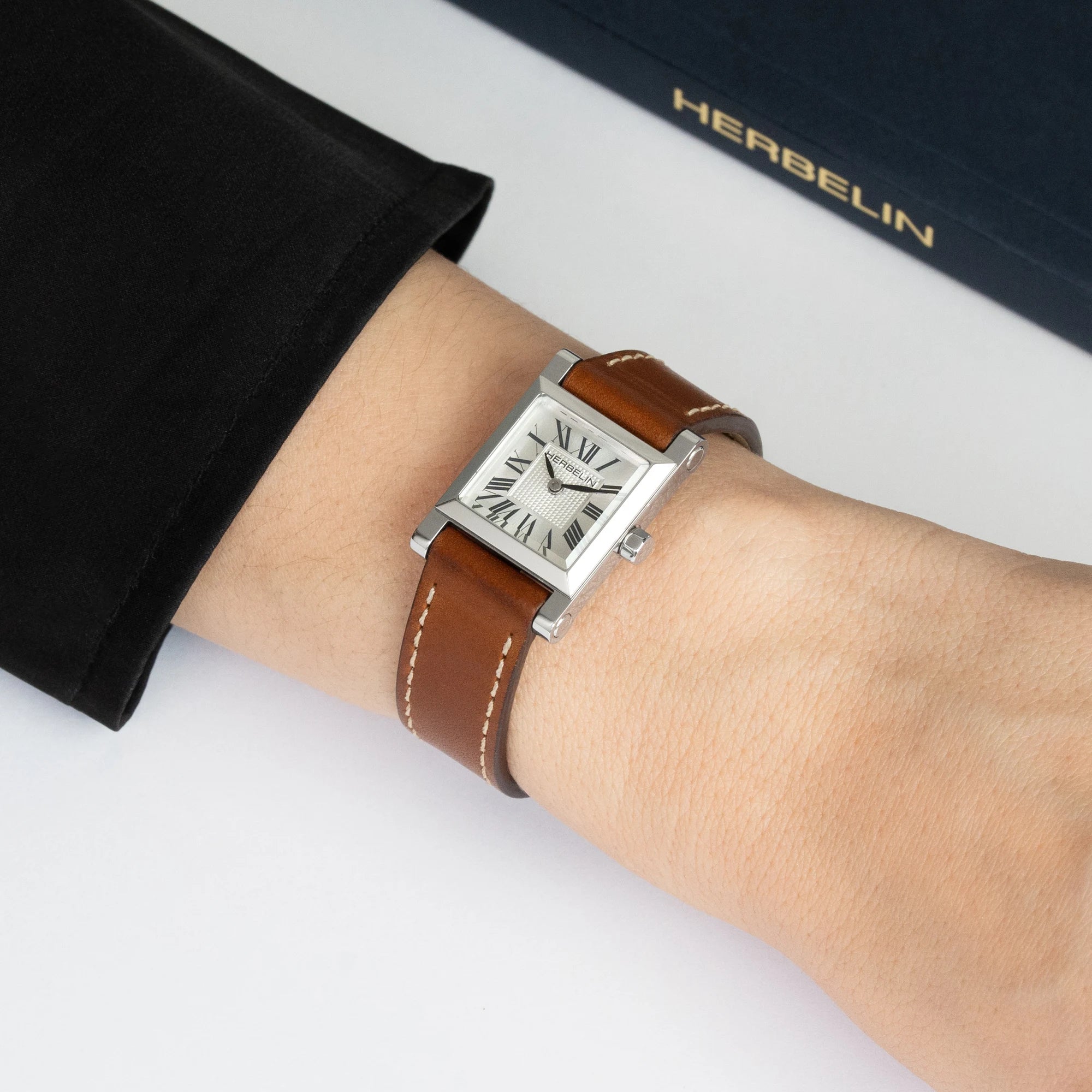 Au poignet féminin, cadran argenté et bracelet cuir camel visibles
